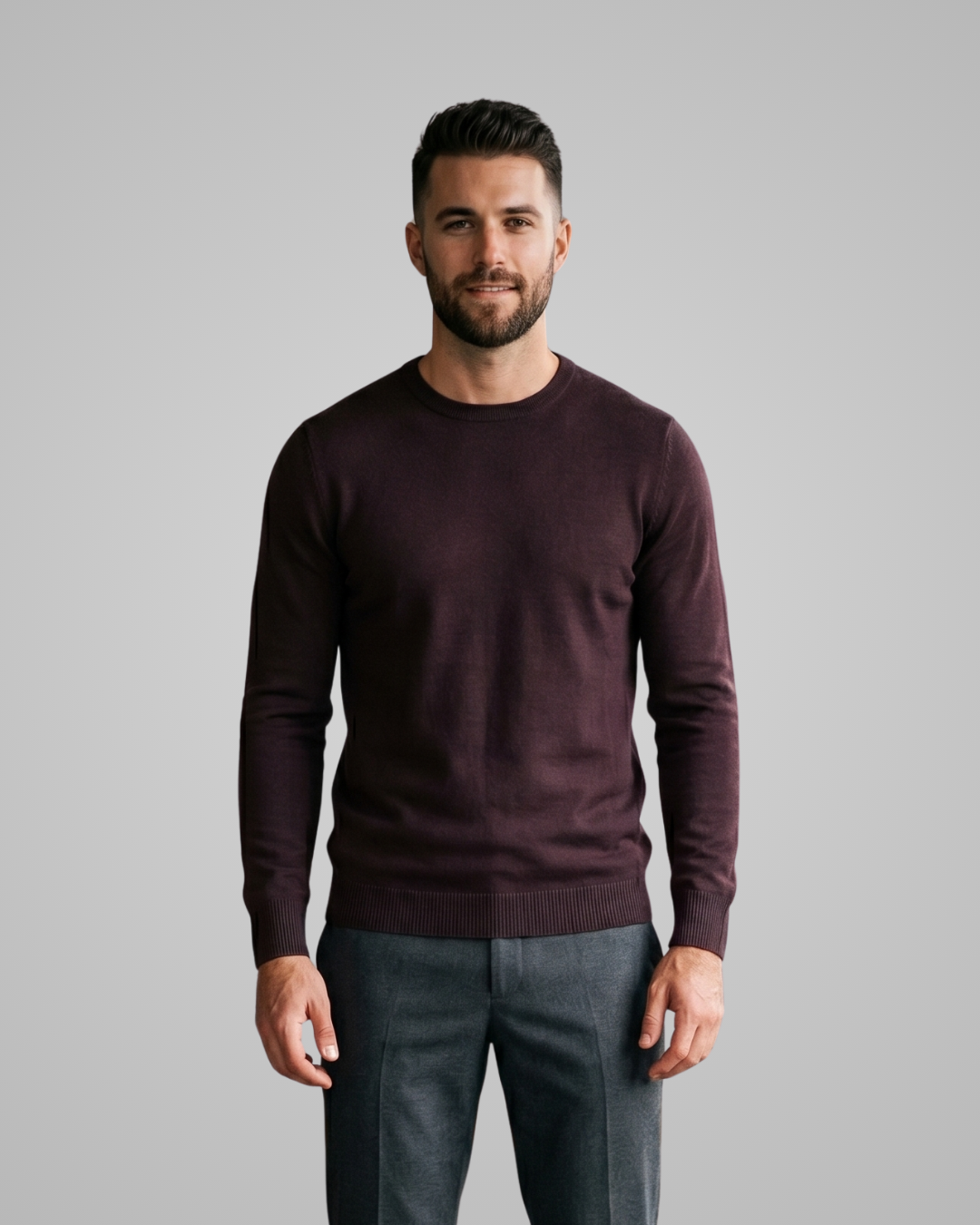Man wearing a maroon sweater and gray pants against a gray background