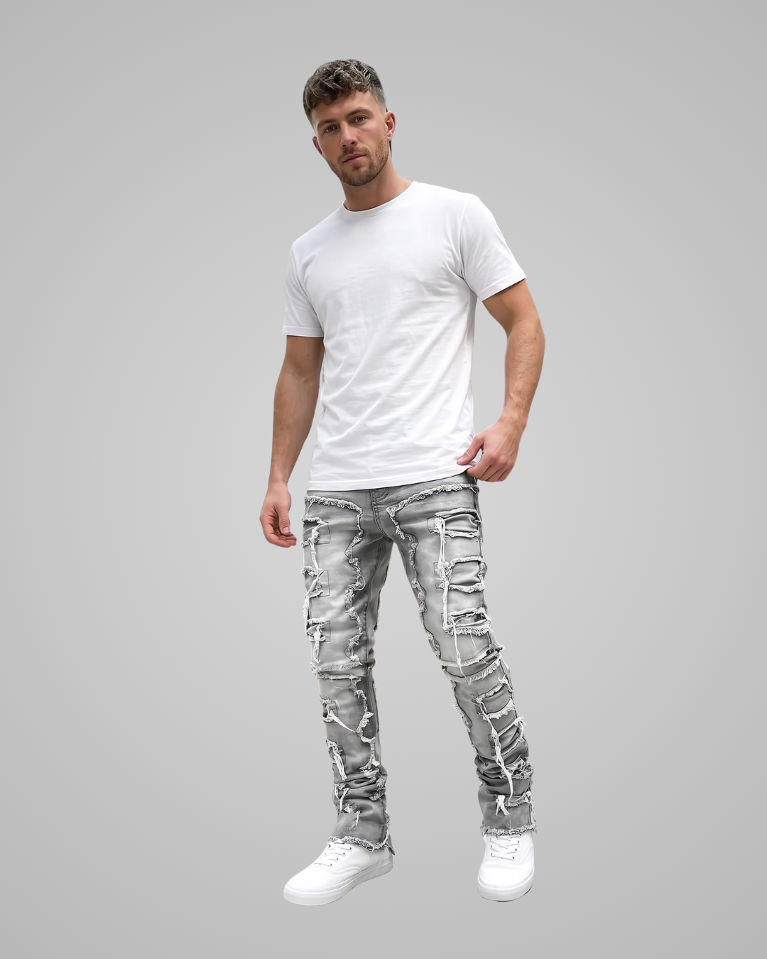 A man modeling distressed light gray skinny jeans with ripped details, paired with a plain white t-shirt and white sneakers, set against a solid gray background.
