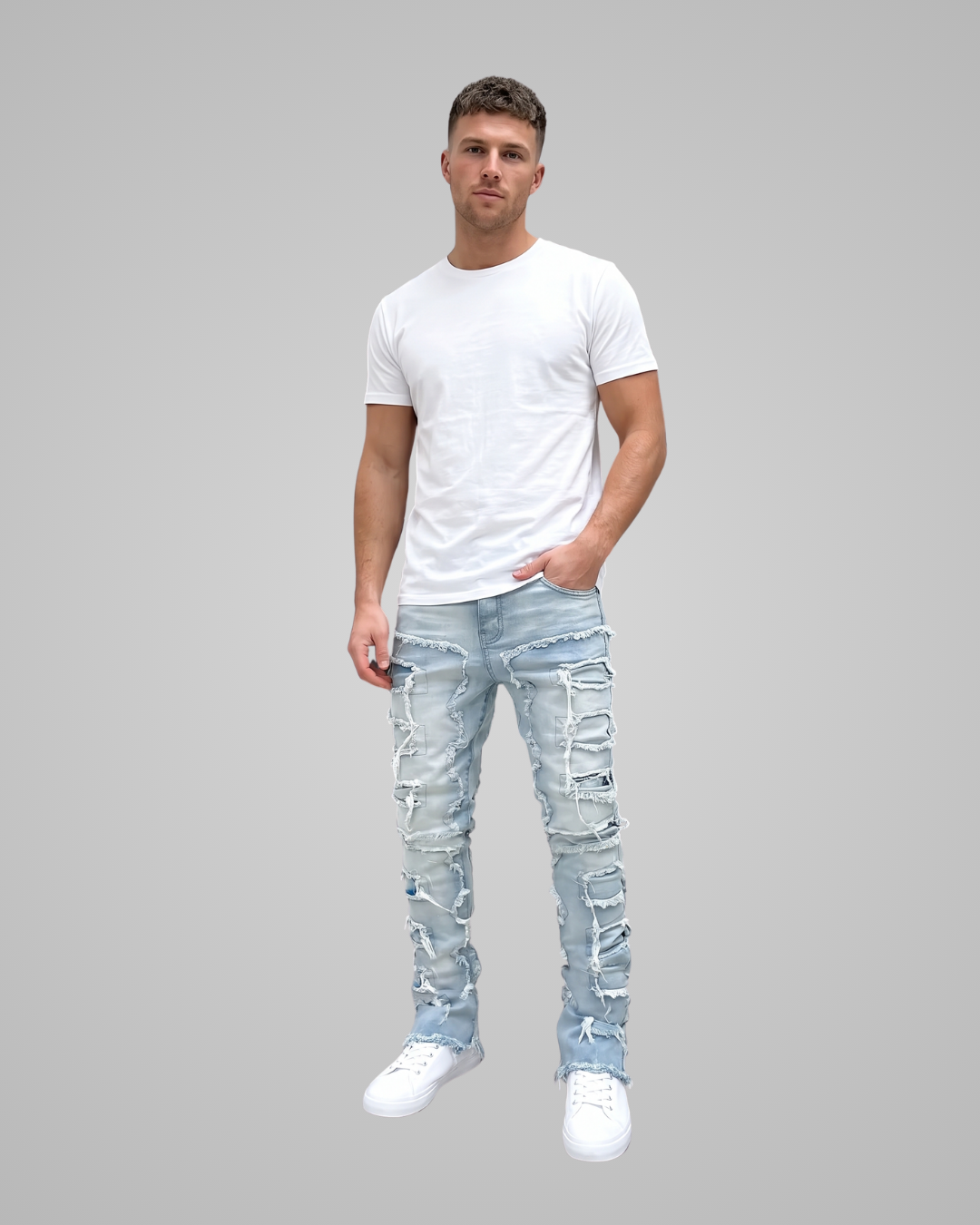 A man modeling a pair of light blue, heavily distressed and ripped skinny jeans, paired with a plain white t-shirt and white sneakers, against a solid gray background.