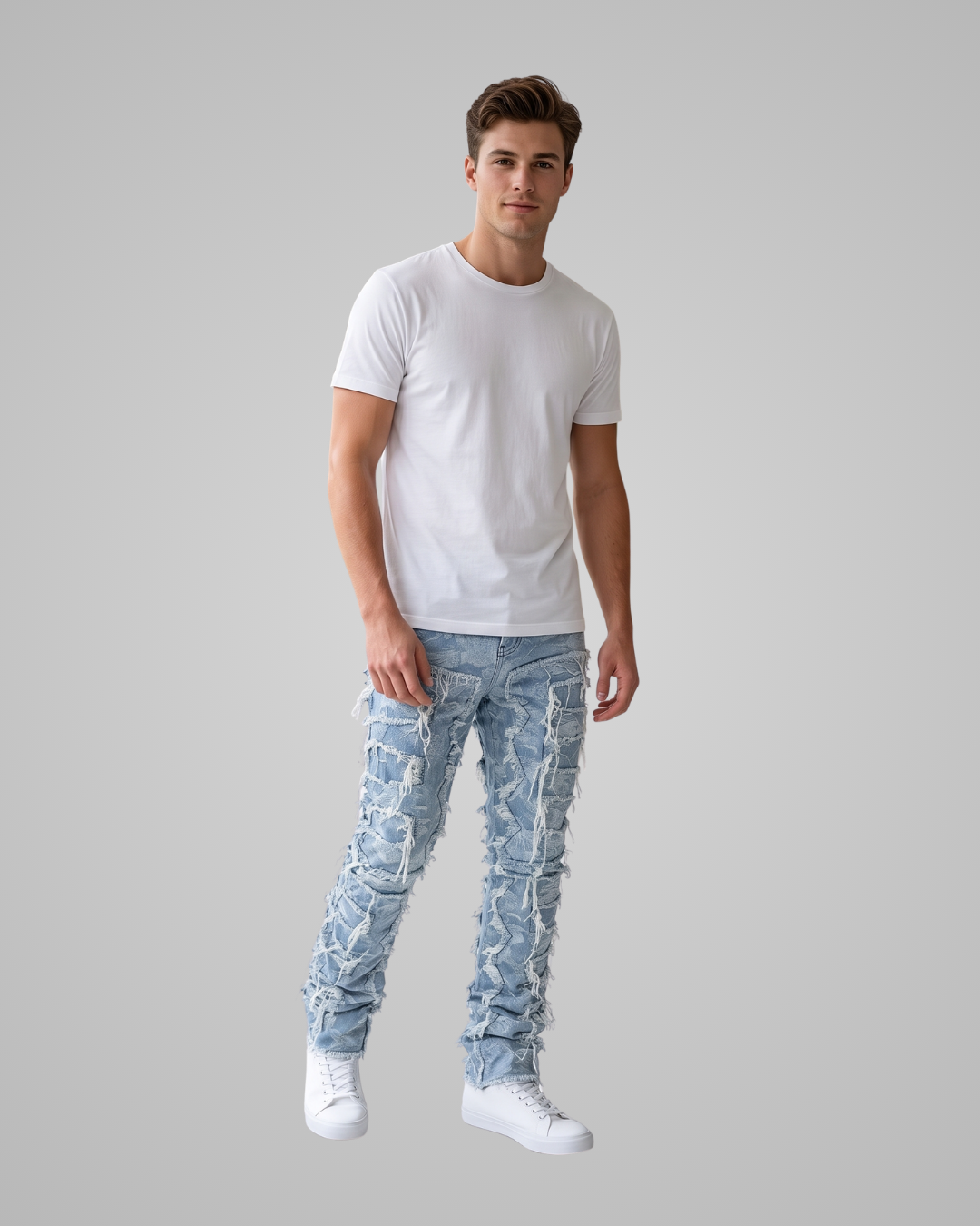 A man modeling a pair of light blue ripped denim jeans with a white t-shirt and white sneakers, set against a solid gray studio background.