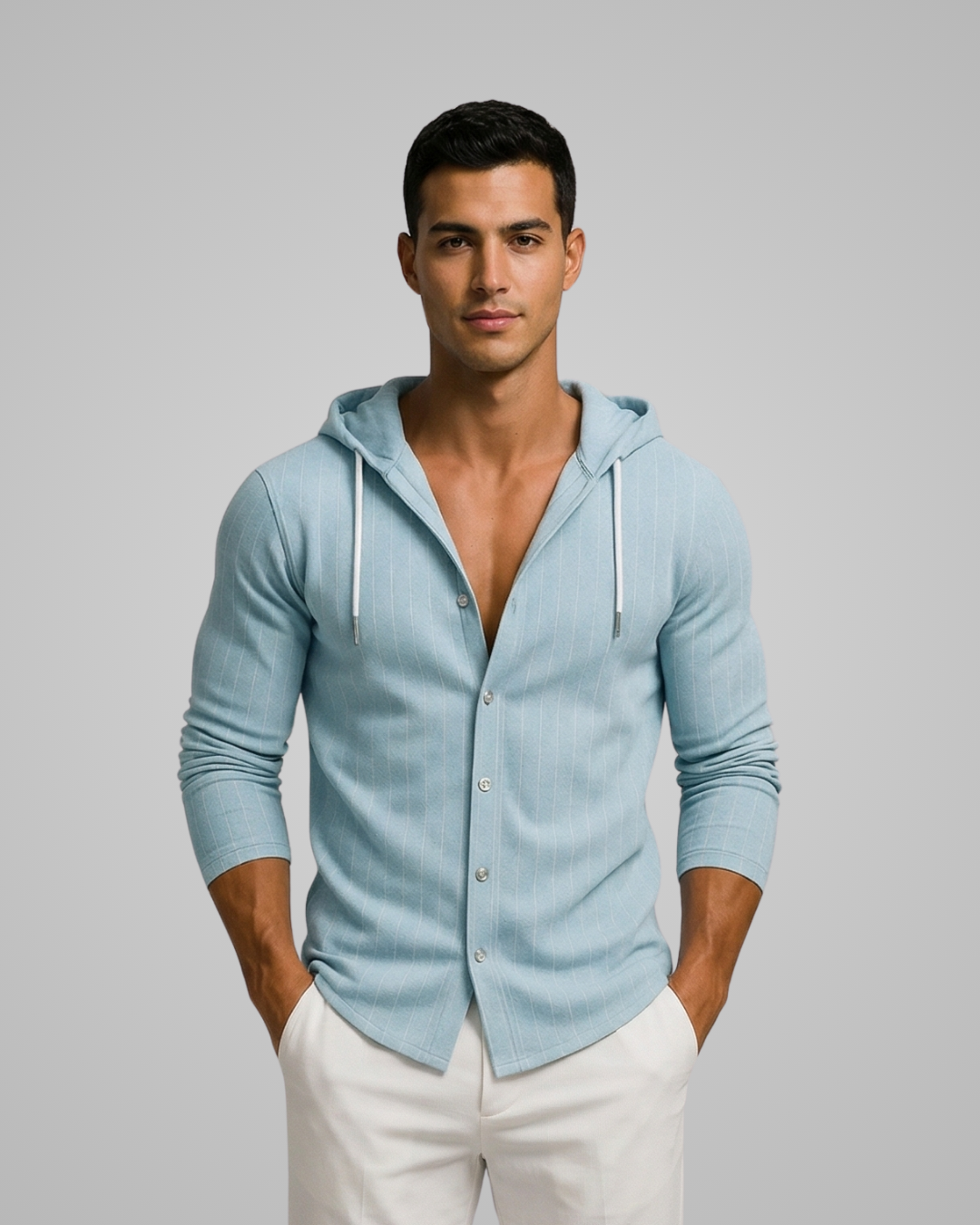 Man wearing a light blue hoodie over a shirt with white pants on a gray background