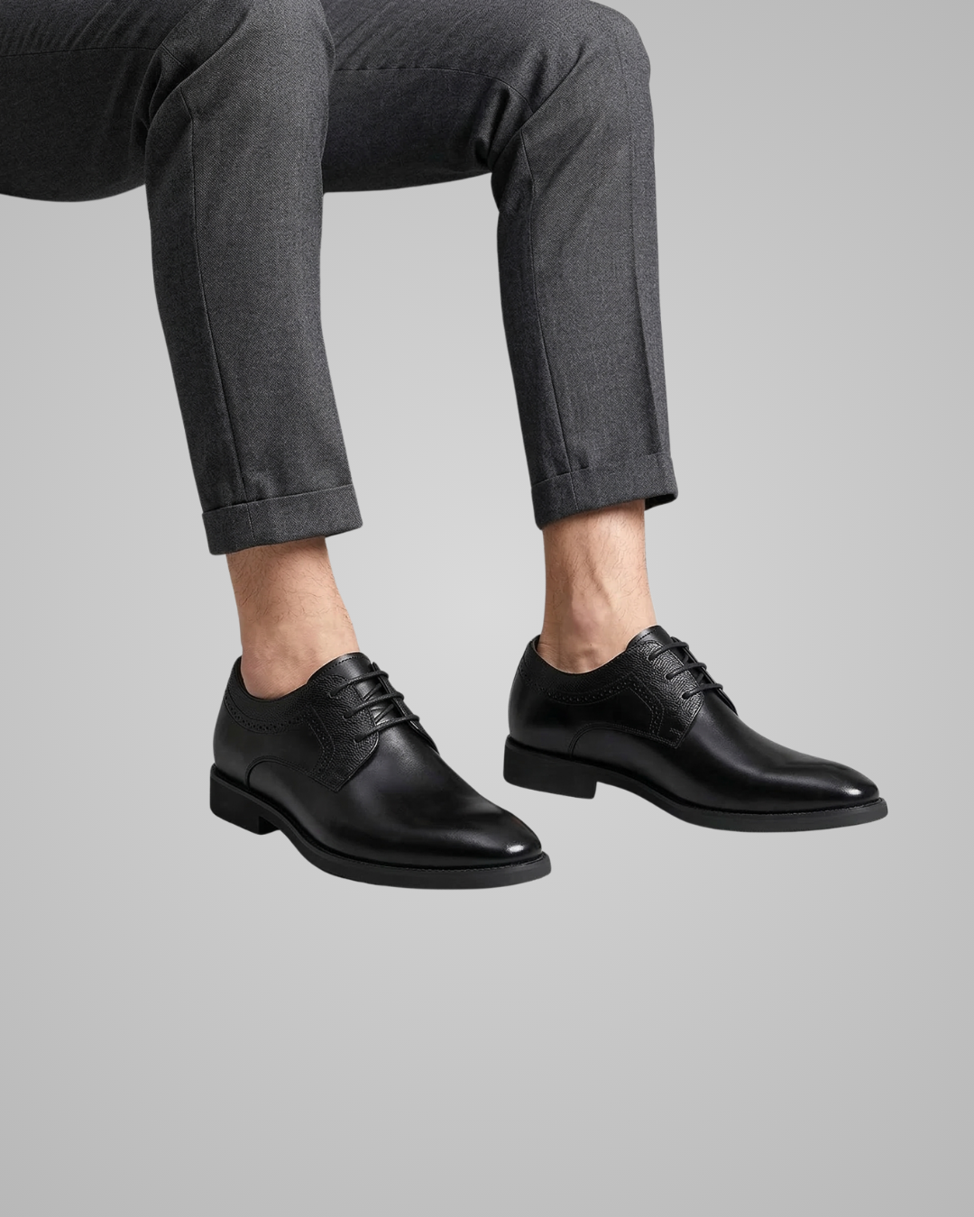 Person wearing black dress shoes and gray pants on a light gray background