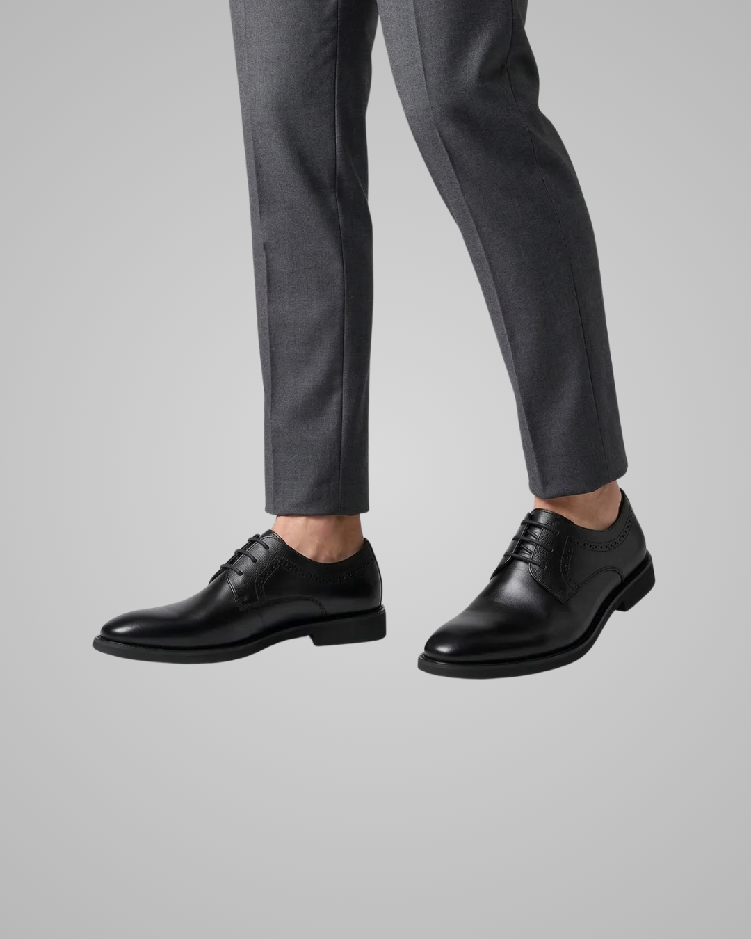 Black dress shoes worn with gray pants on a light gray background