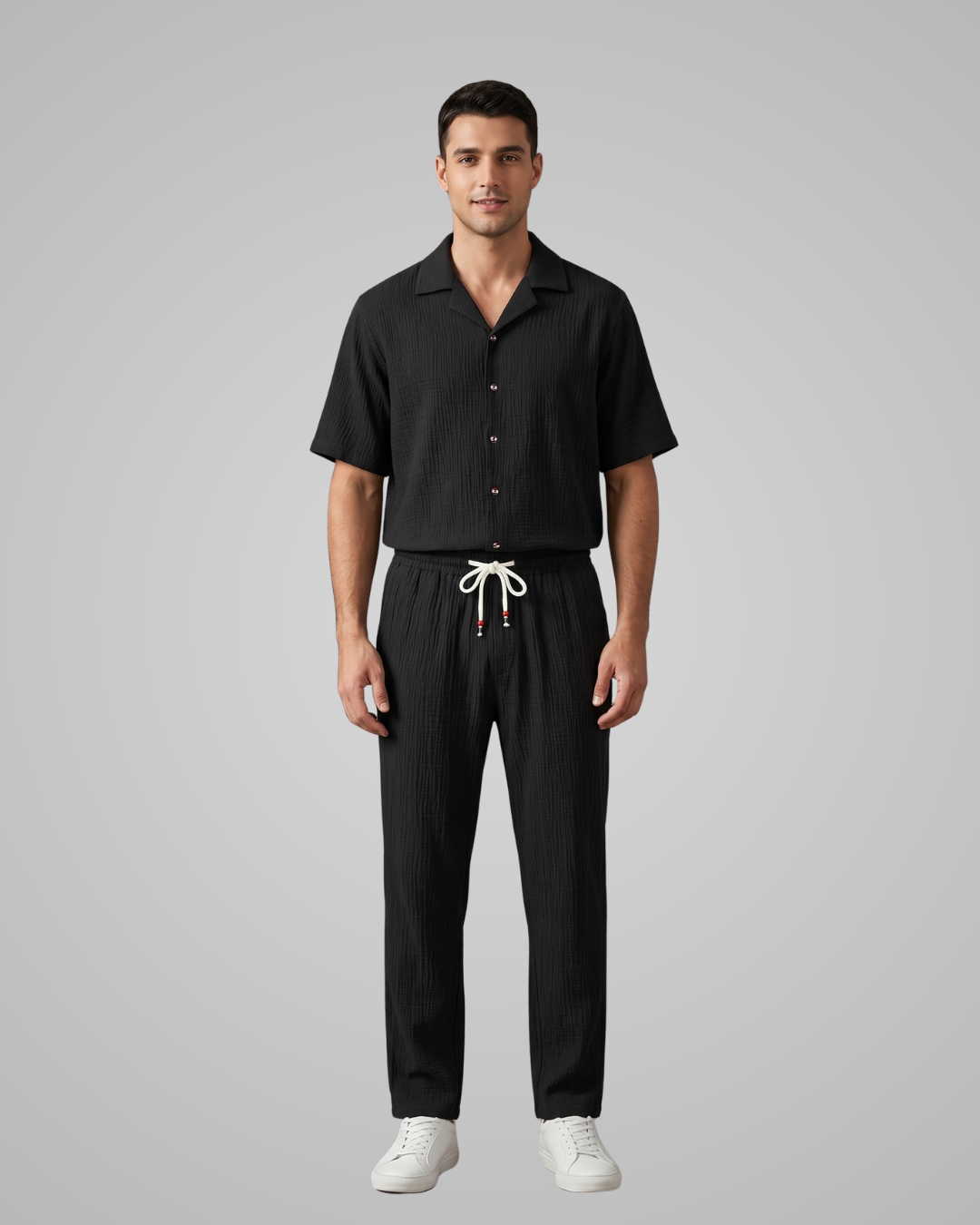 Man wearing a black shirt and black pants with white shoes on a gray background