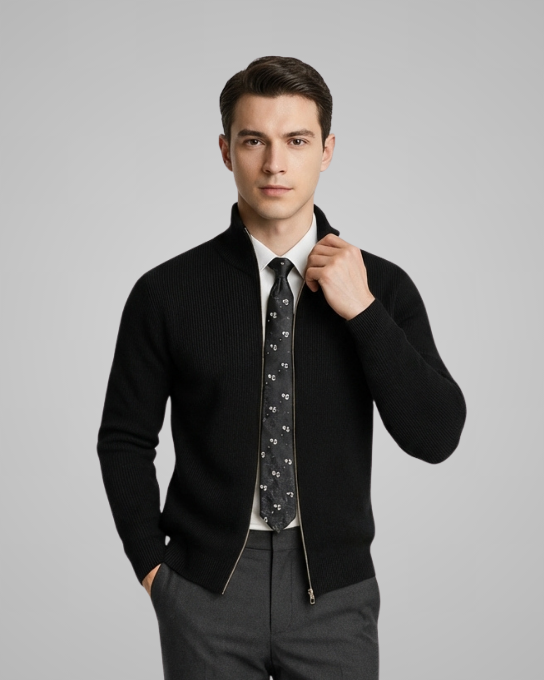 Man wearing a black sweater over a white shirt with a patterned tie on a gray background