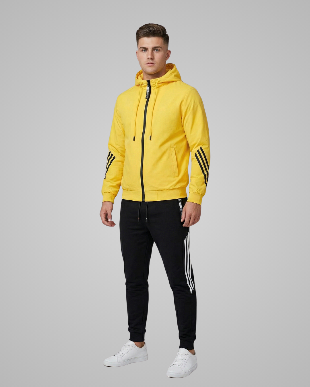 Man wearing a yellow hoodie and black pants with white stripes on a gray background