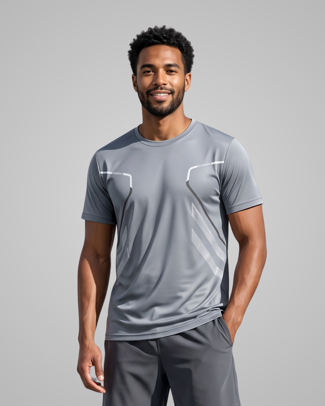 A man wearing a gray short-sleeve athletic t-shirt with white geometric accents on the chest, paired with matching gray athletic pants, set against a solid gray studio background.