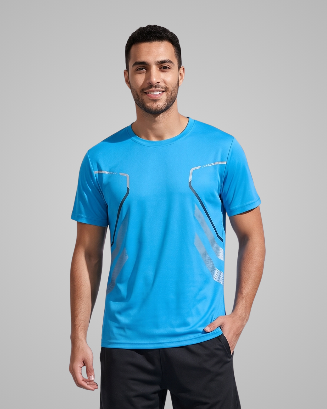 A man wearing a bright blue athletic t-shirt with gray geometric line patterns on the chest, paired with black athletic pants, standing against a solid gray studio background.
