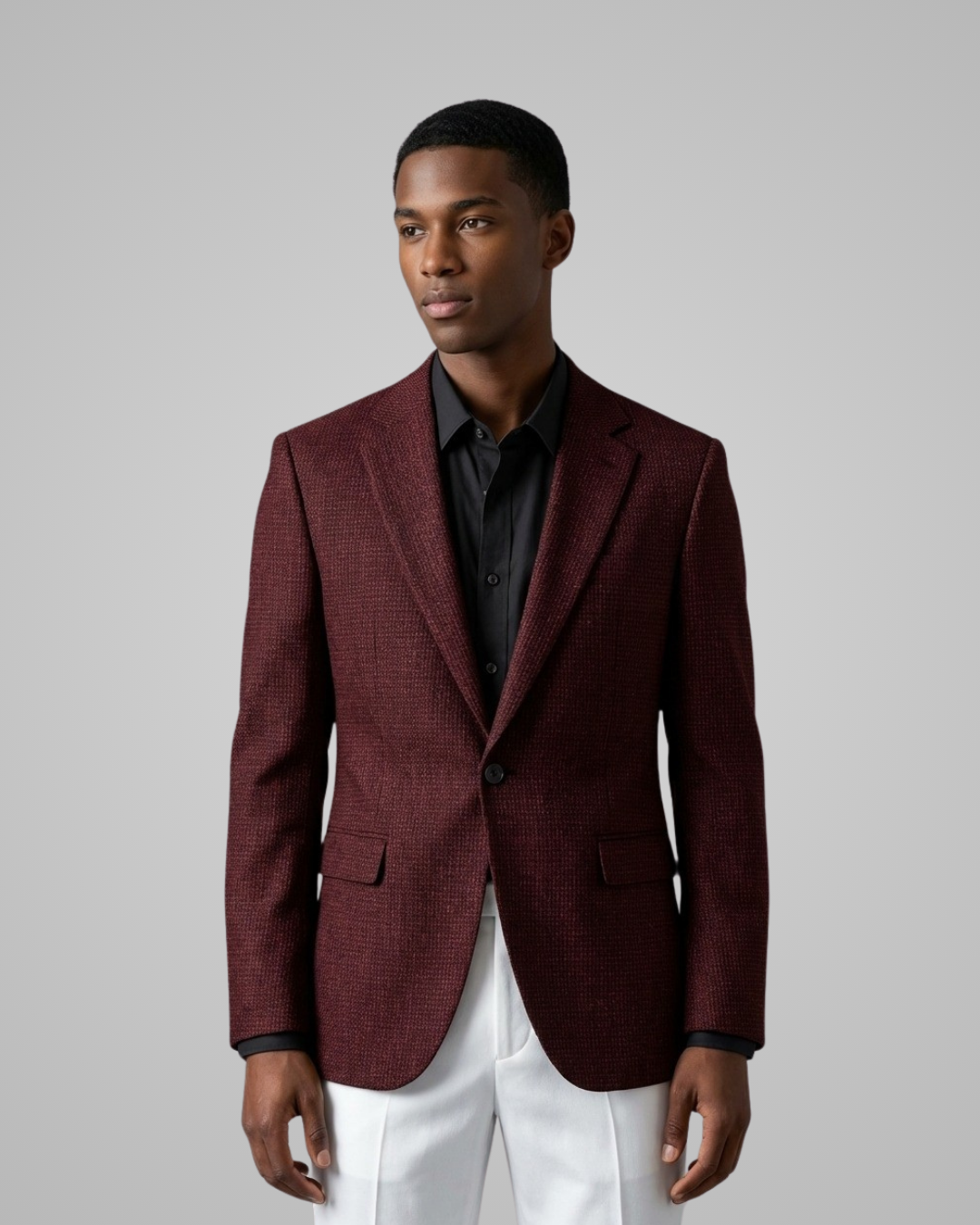 Man wearing a burgundy blazer over a black shirt with white pants on a gray background