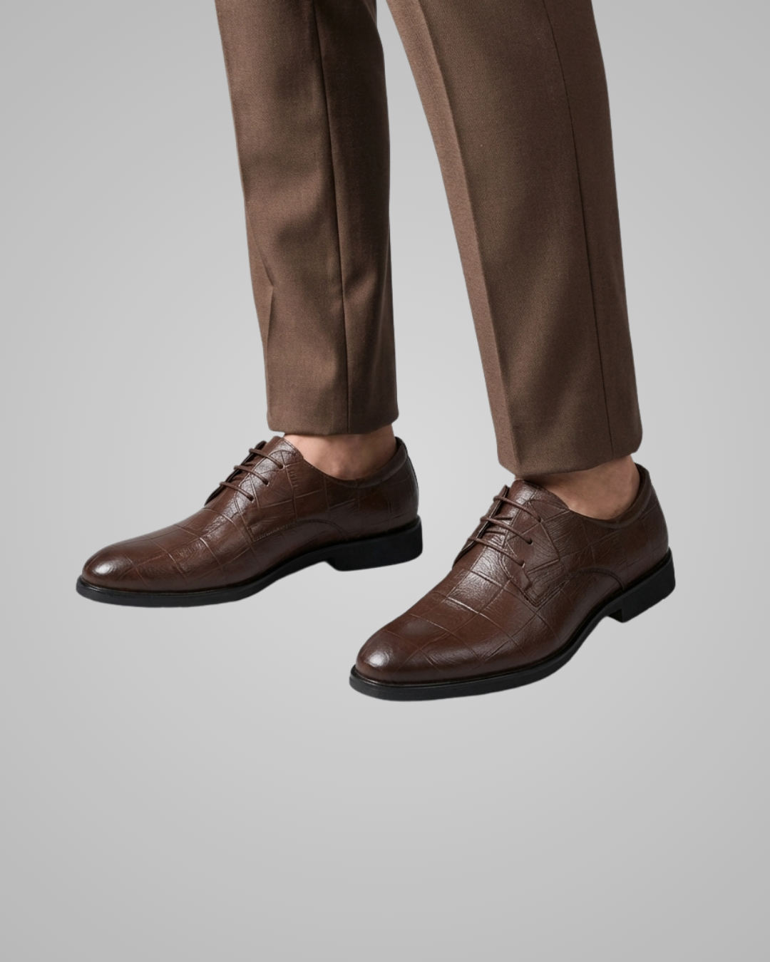 Brown dress shoes worn with brown pants on a gray background