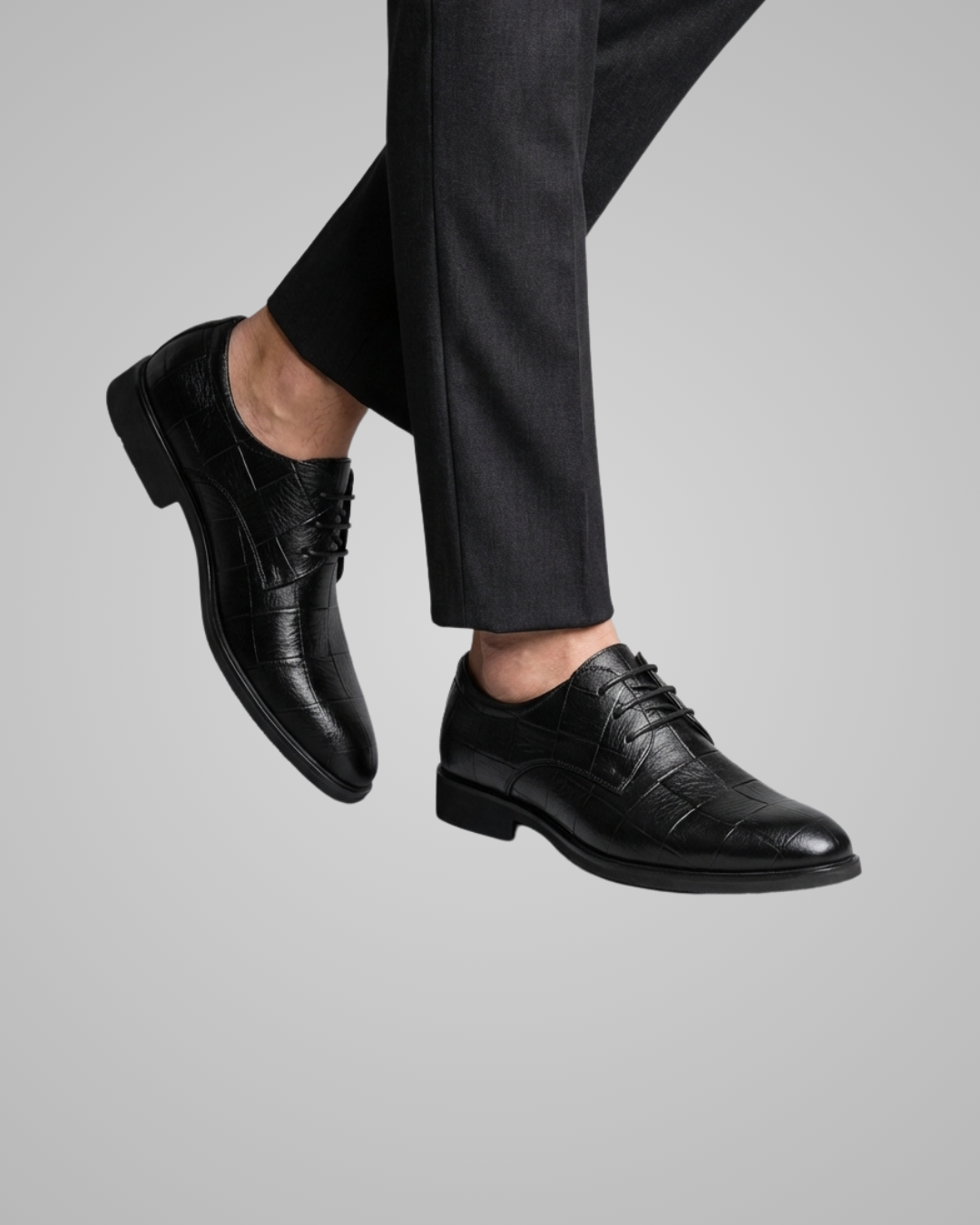 Black dress shoes worn with black pants on a gray background