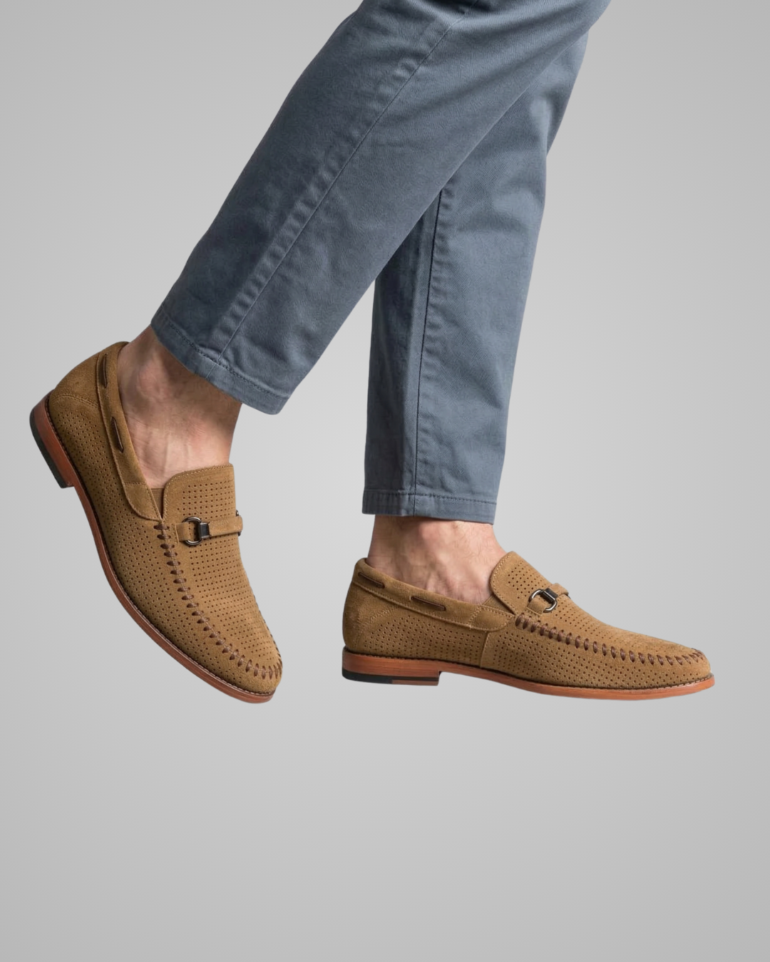 Brown loafers worn with light blue jeans on a gray background