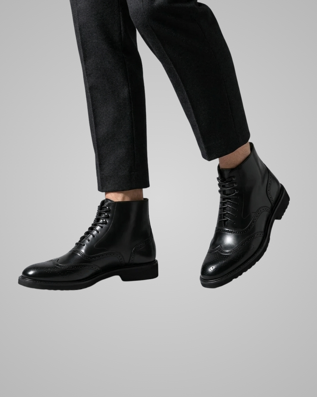 Black leather boots worn with black pants on a gray background