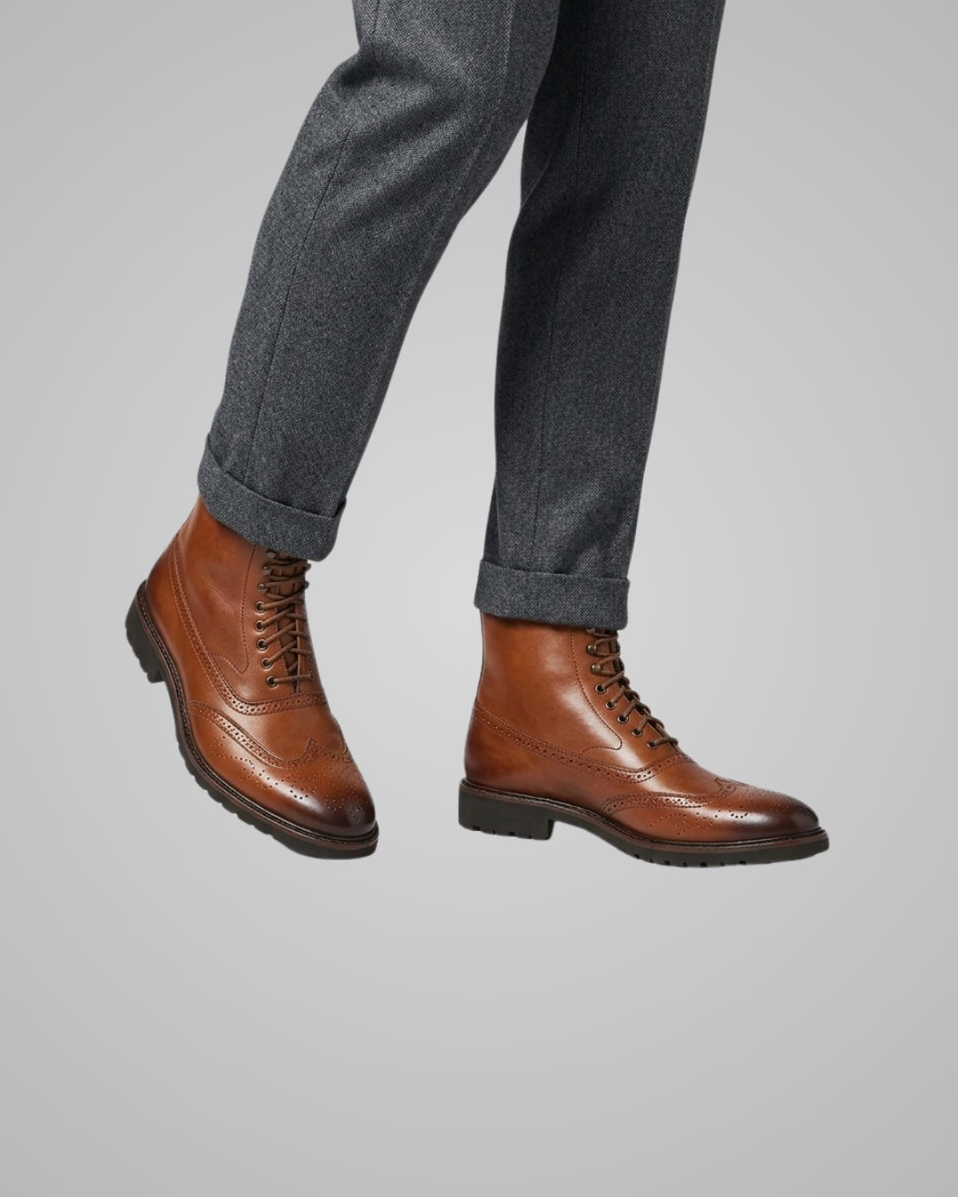 Brown leather boots worn with gray pants on a light gray background