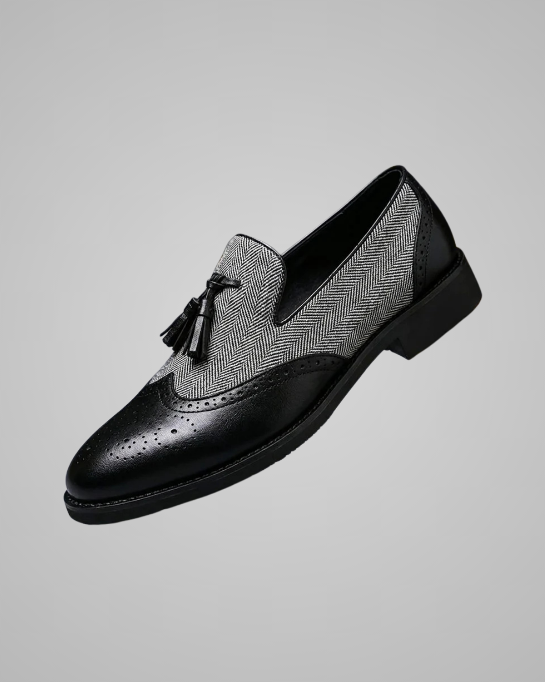 A men's slip-on wingtip shoe featuring a black leather toe cap with brogue perforations, a black leather heel, and a black-and-white herringbone patterned upper panel with a black tassel detail.