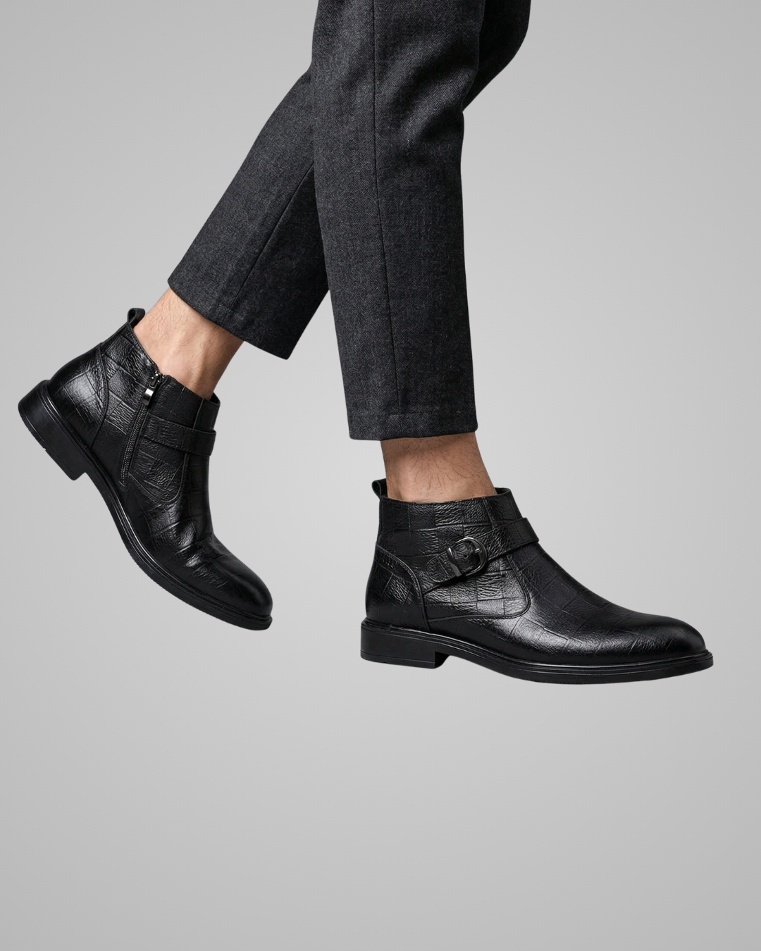 Black leather boots worn with dark pants on a gray background