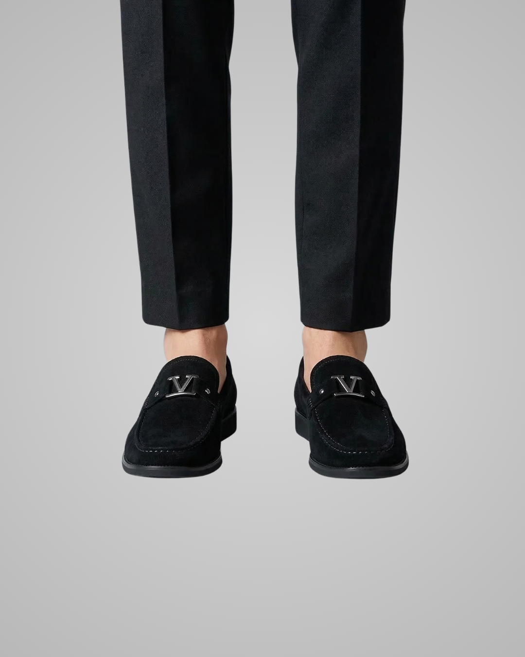 Black loafers with a logo worn with black pants on a gray background