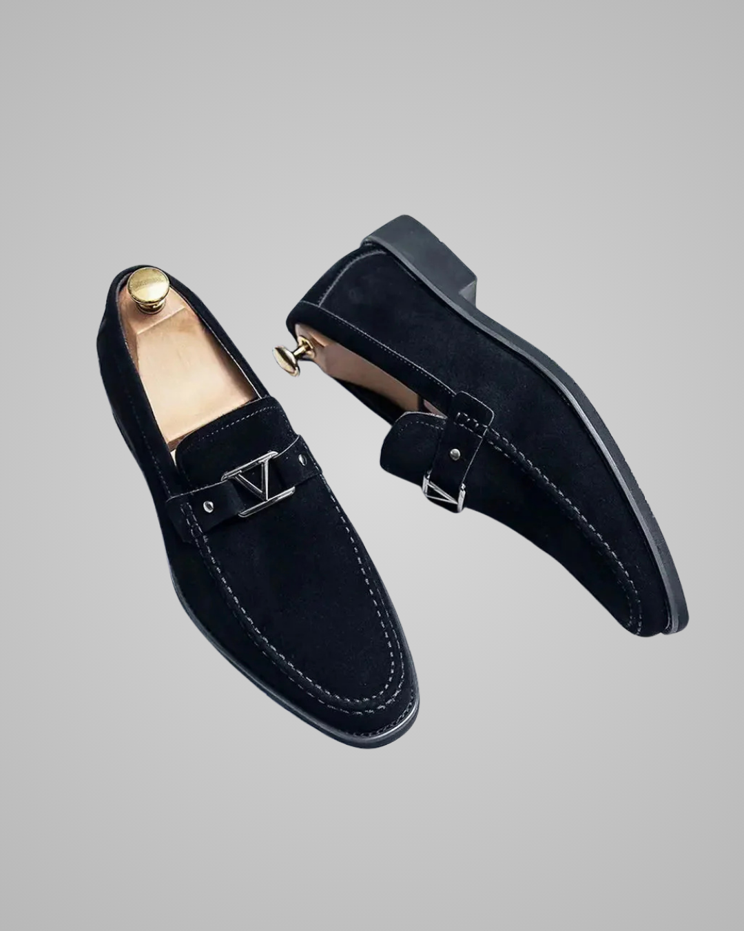 Pair of black loafers with gold buckles on a gray background