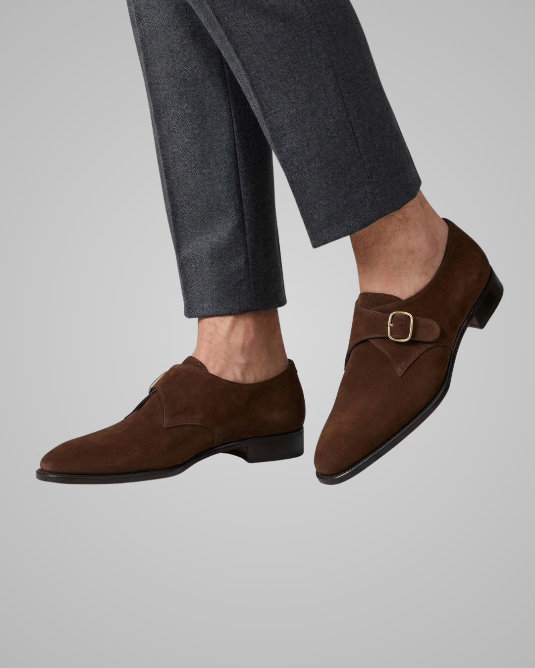 Brown loafers with a buckle on gray pants against a light gray background