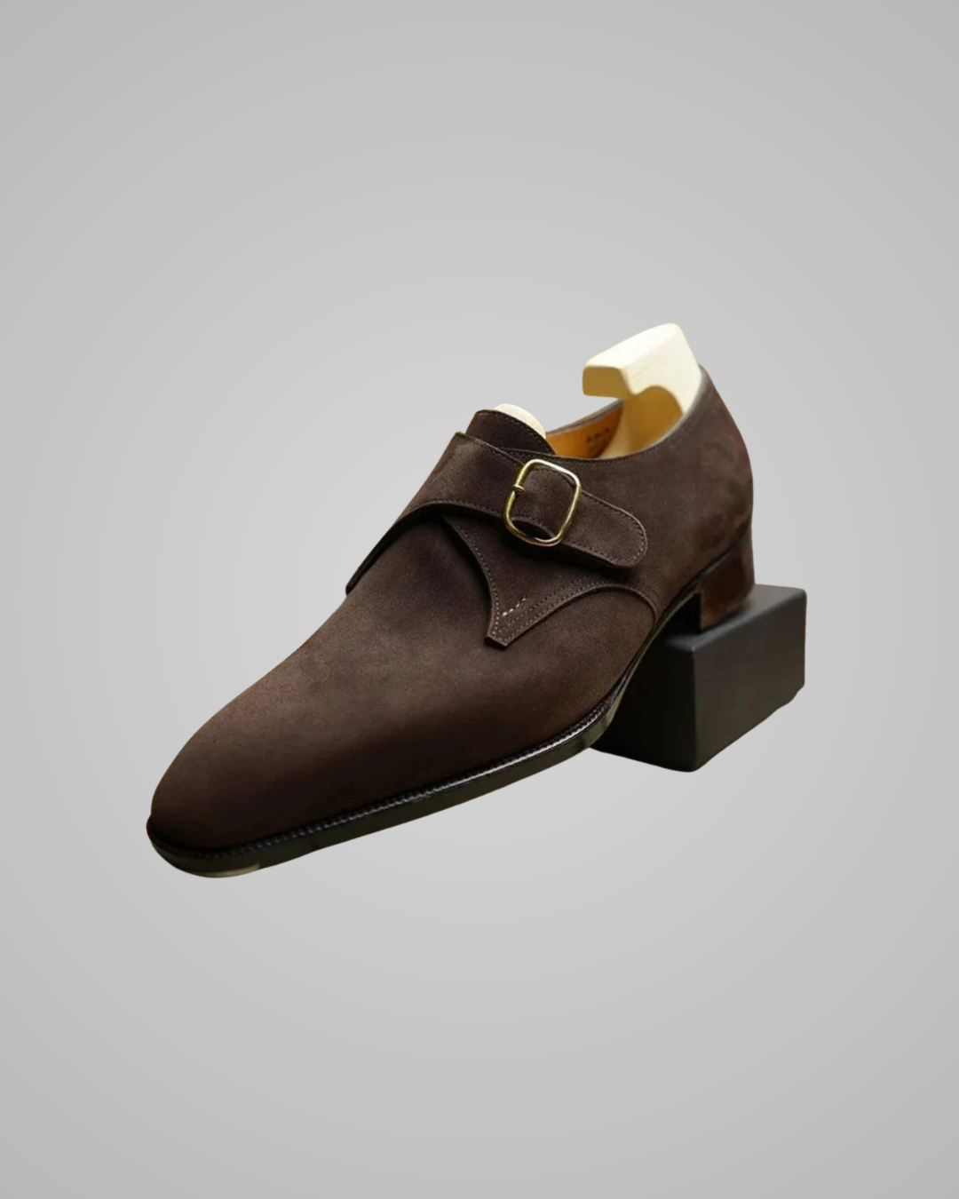 Brown suede shoe with a buckle on a gray background