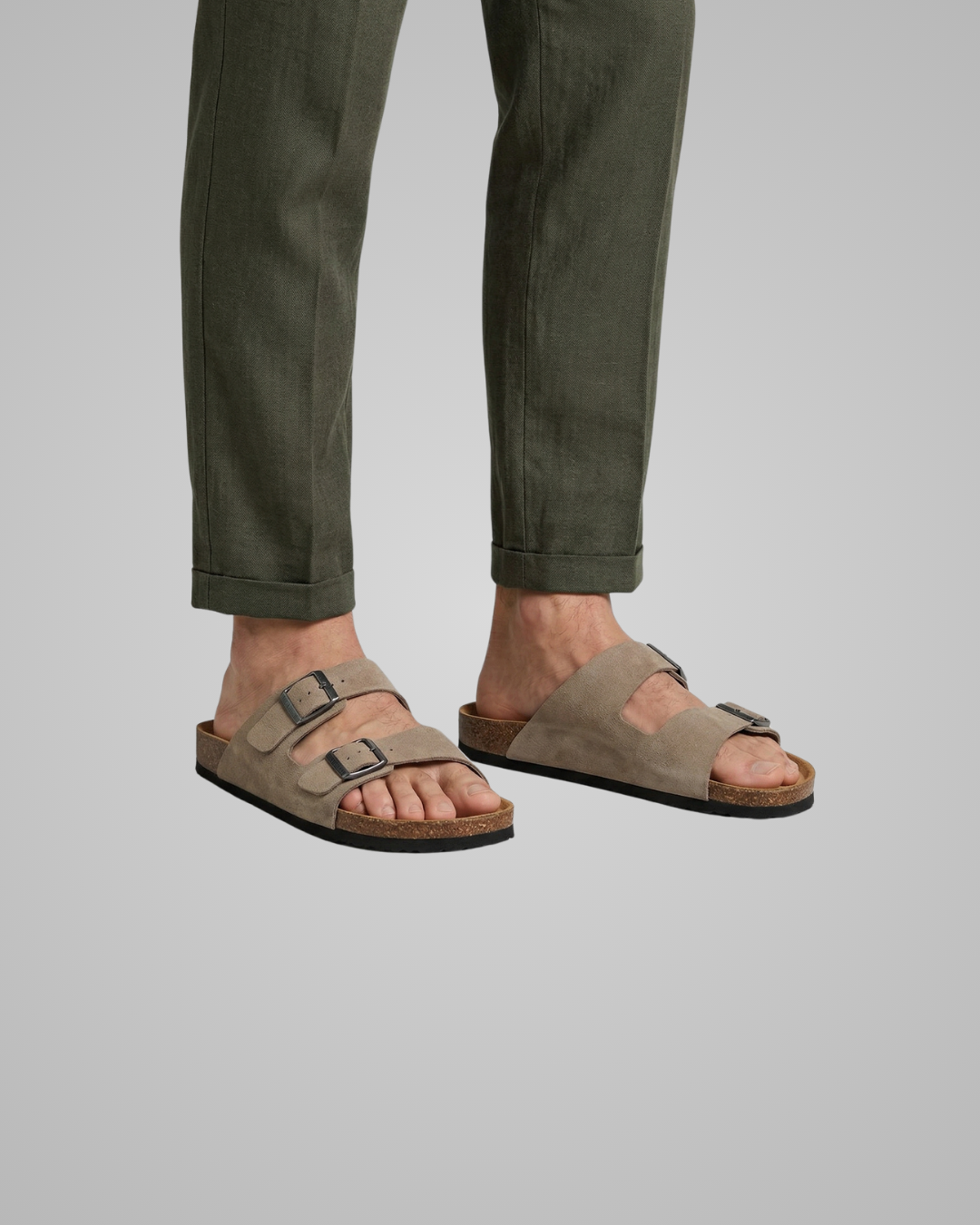 Person wearing brown sandals and green pants on a plain background