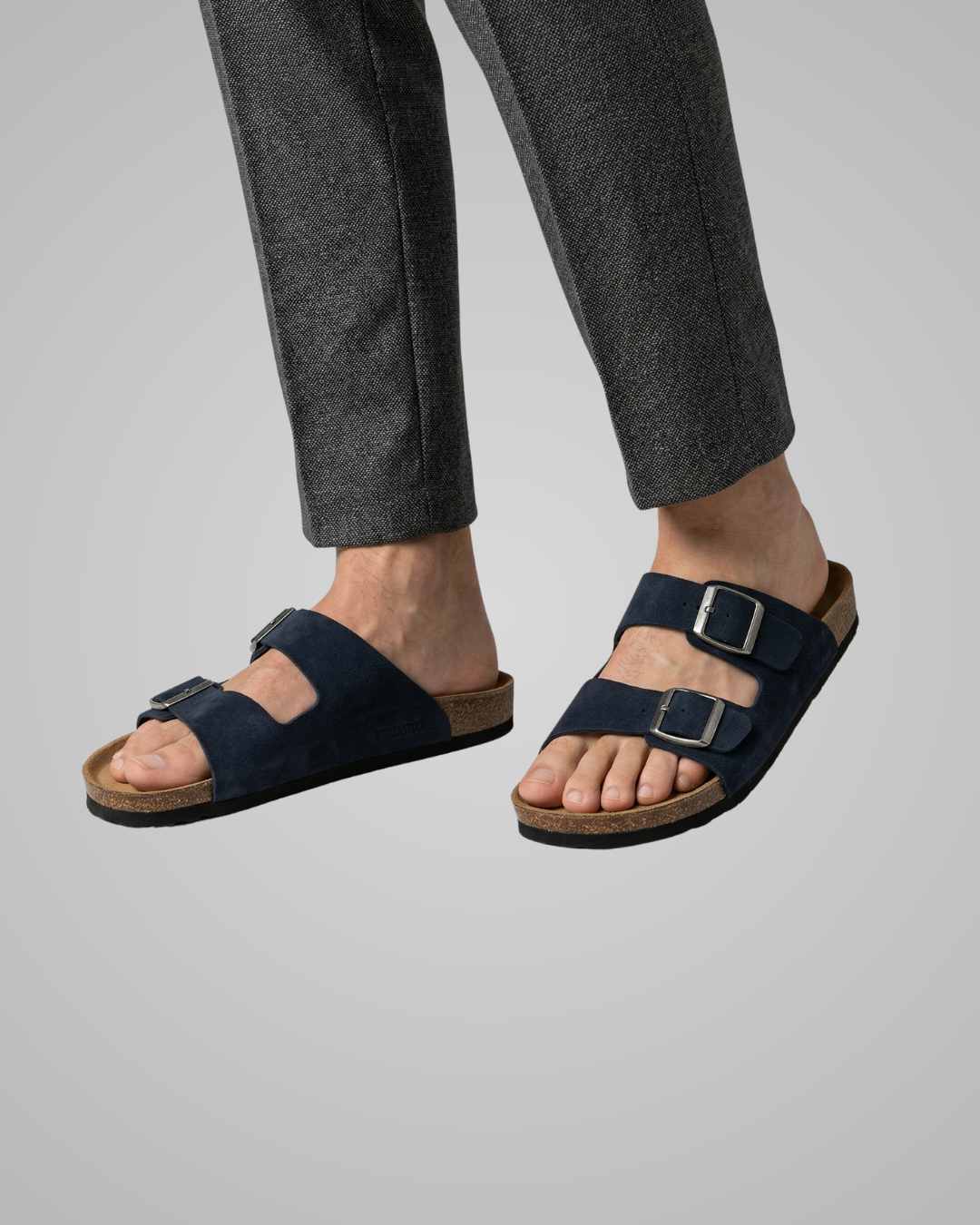 Navy sandals worn with gray pants on a plain background