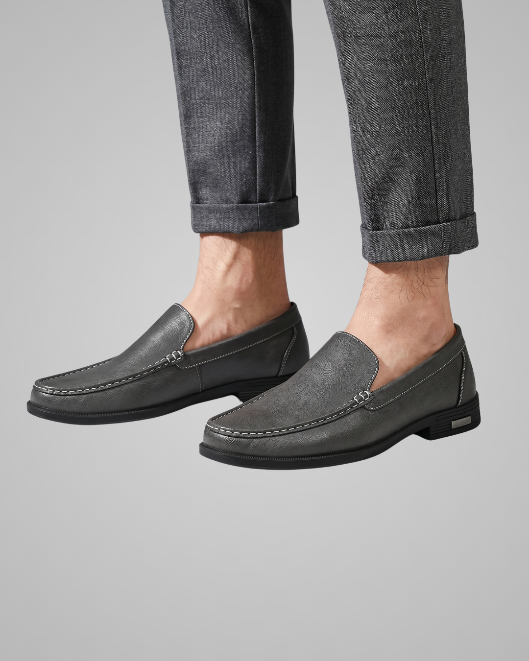 Gray loafers worn with rolled-up jeans on a gray background