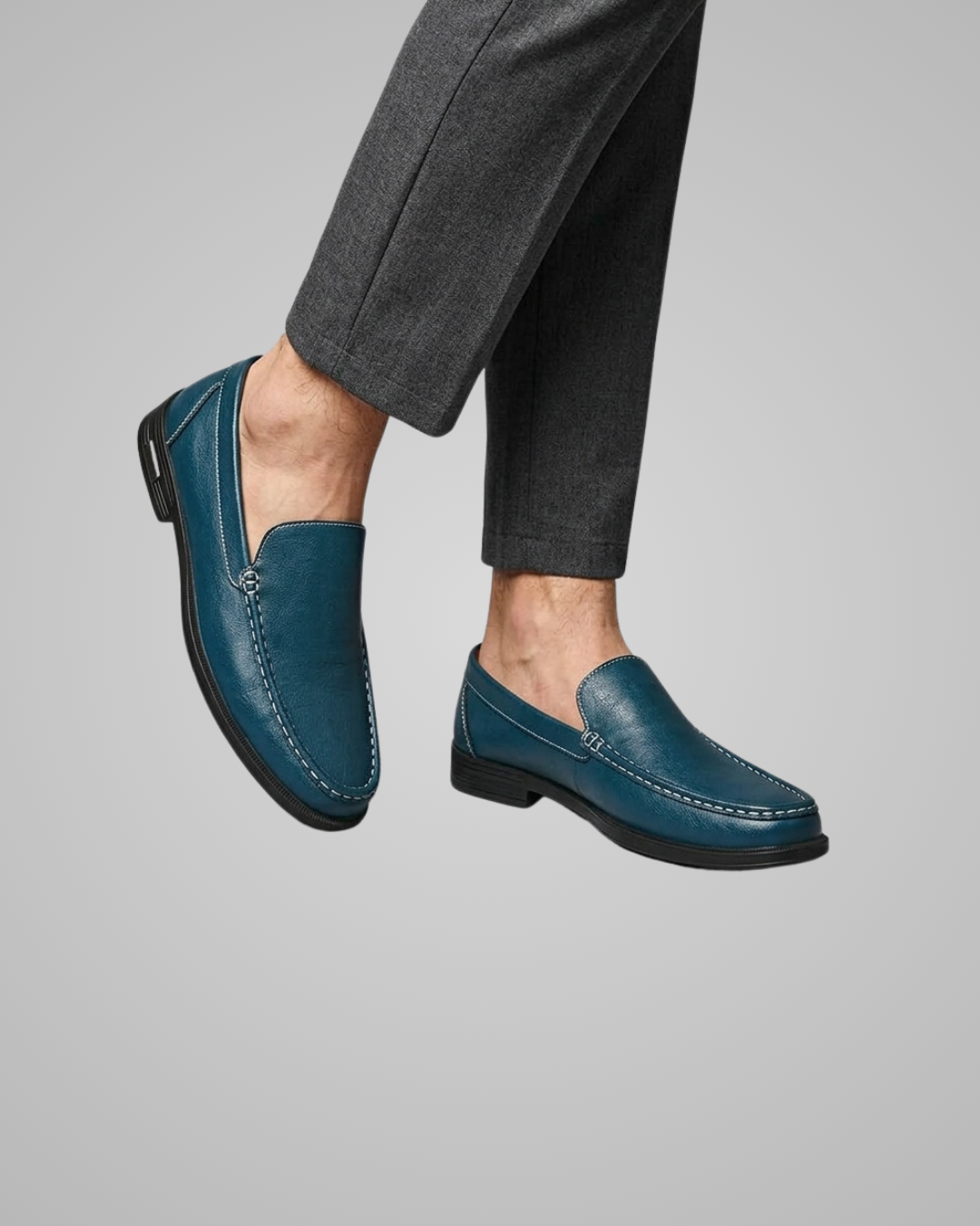 Blue loafers worn with gray pants on a plain background