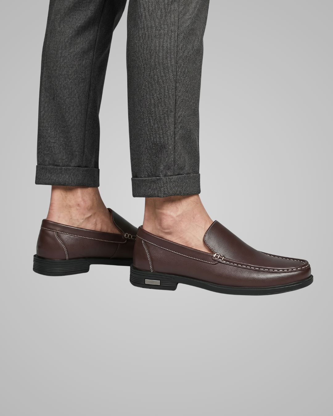 Brown loafers worn with gray pants on a light gray background