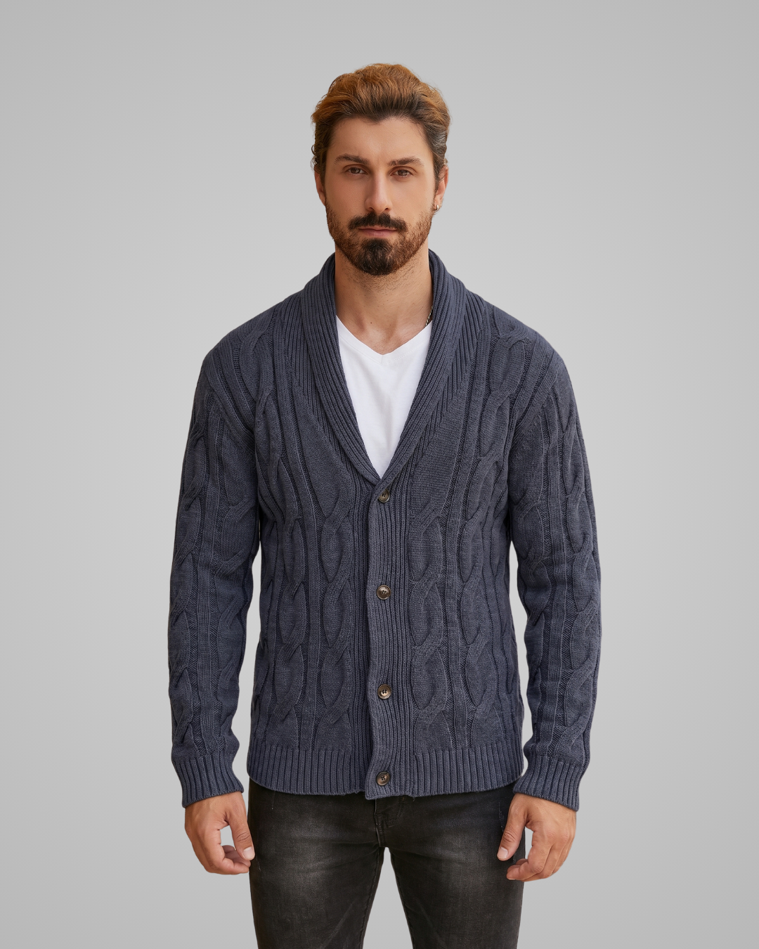 Man wearing a cable knit cardigan over a white shirt on a gray background