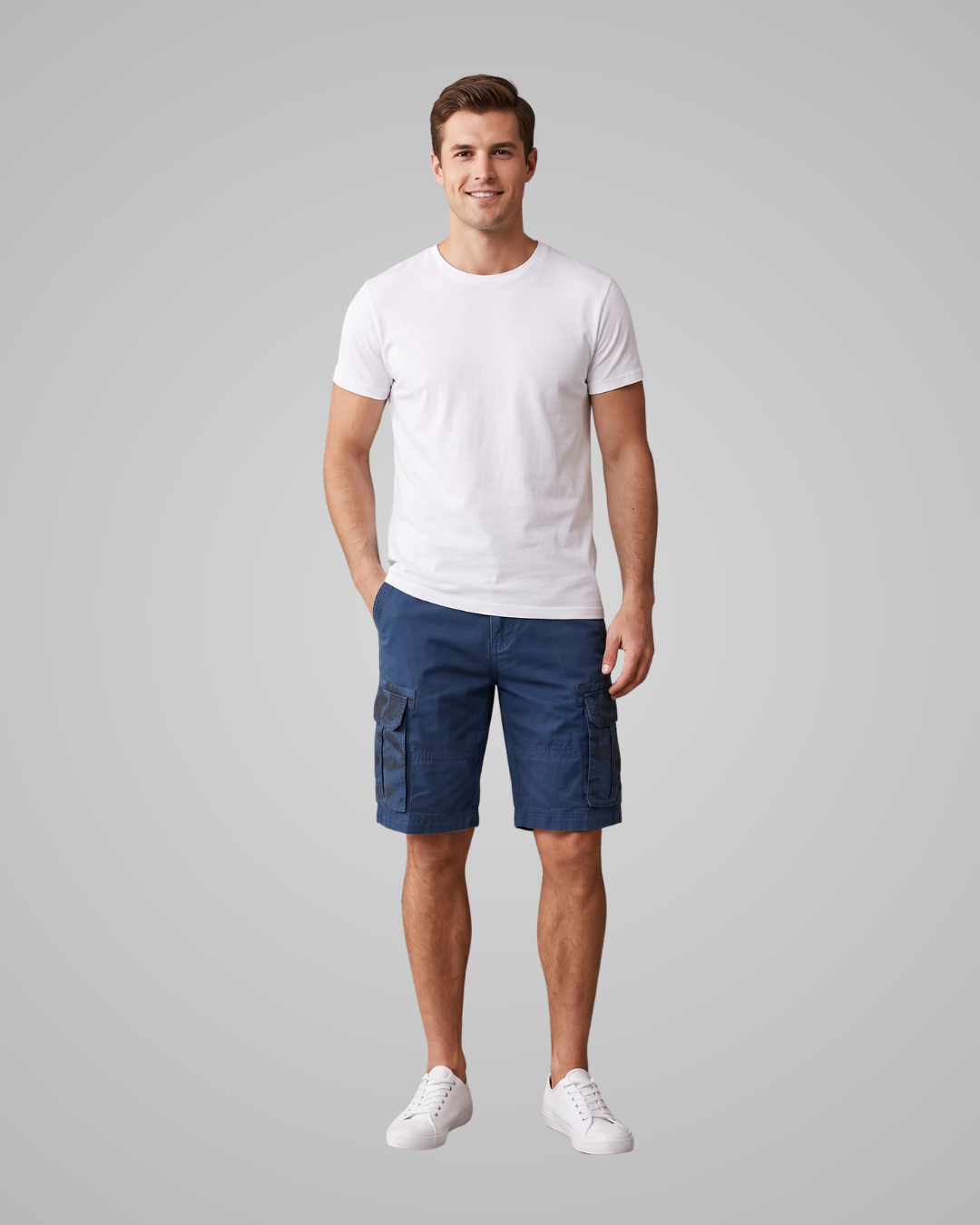 A man modeling a white crew-neck t-shirt and navy blue cargo shorts against a solid gray background.