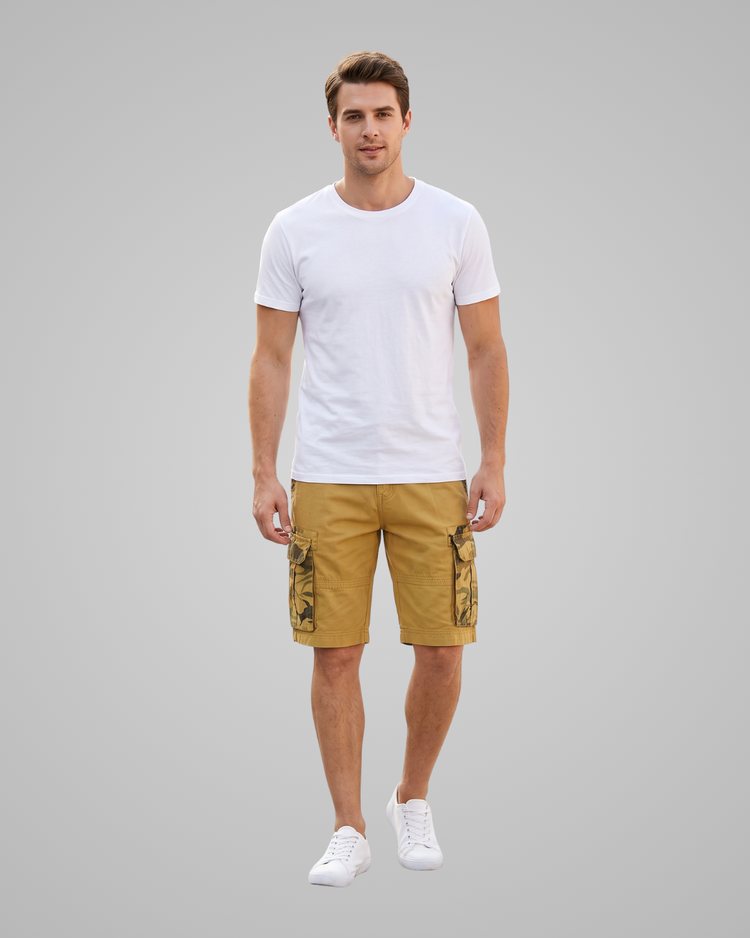 A man modeling a white crew-neck t-shirt and mustard yellow cargo shorts with camouflage details on the side pockets, paired with white sneakers, against a solid gray background.
