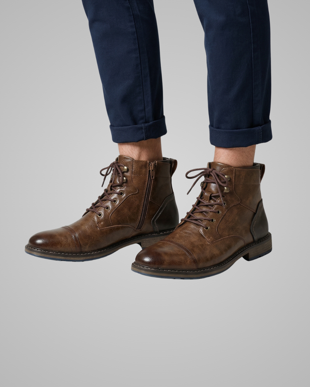 Brown leather boots worn with navy pants on a gray background