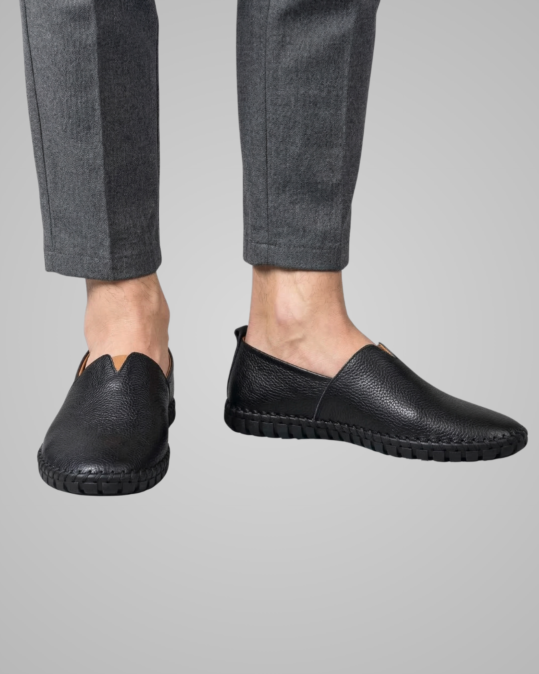 Black leather shoes worn with gray pants on a gray background