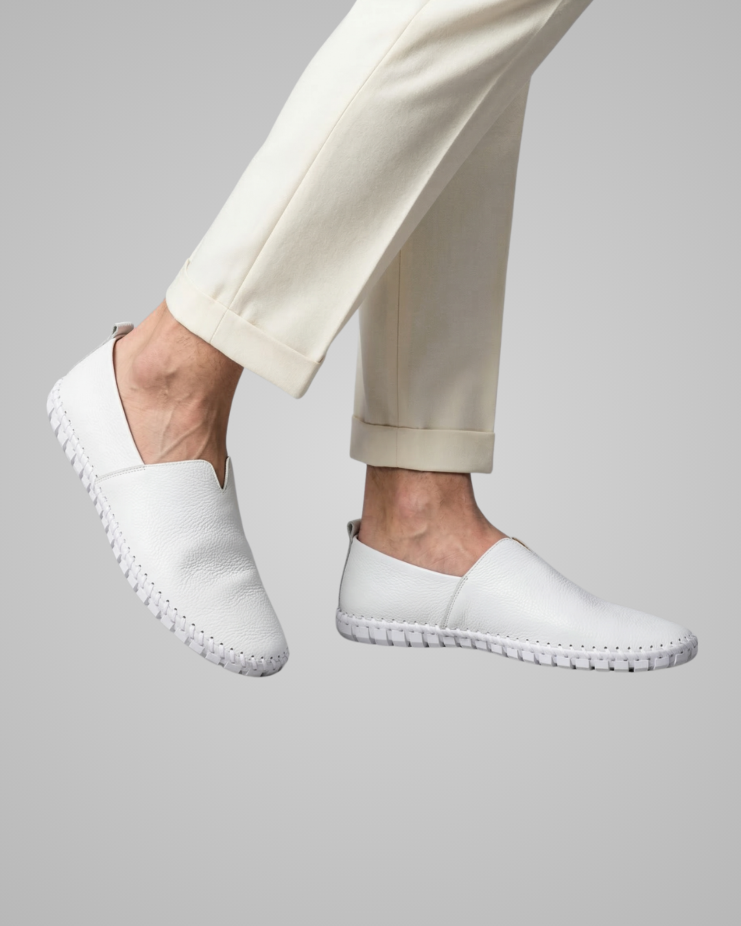 White slip-on shoes worn with beige pants on a light gray background