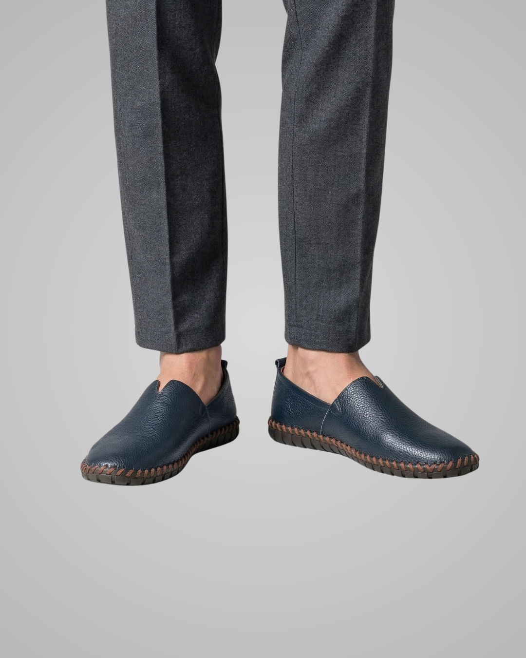 Person wearing navy leather shoes and gray pants on a light gray background