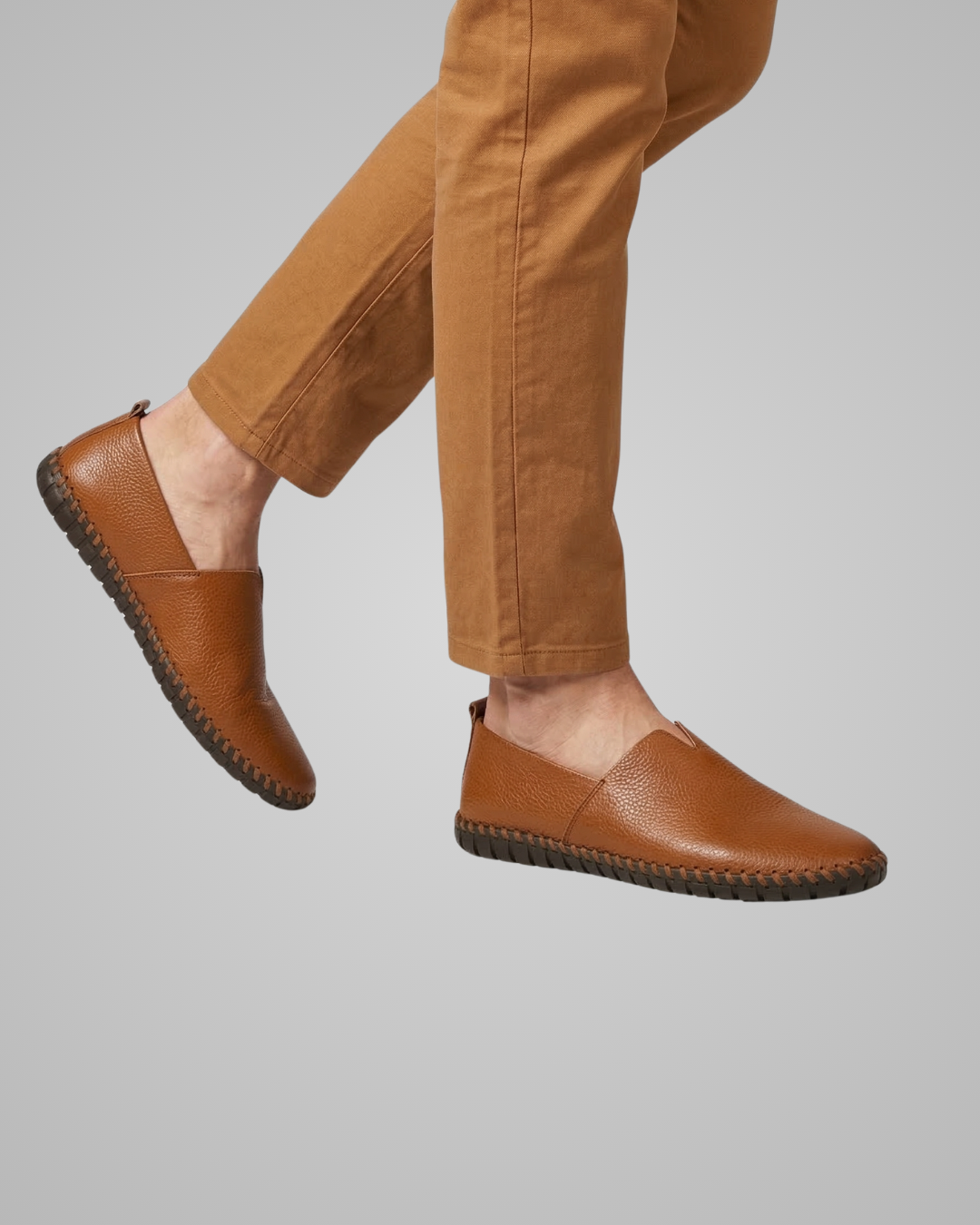 Brown leather shoes worn with brown pants on a gray background