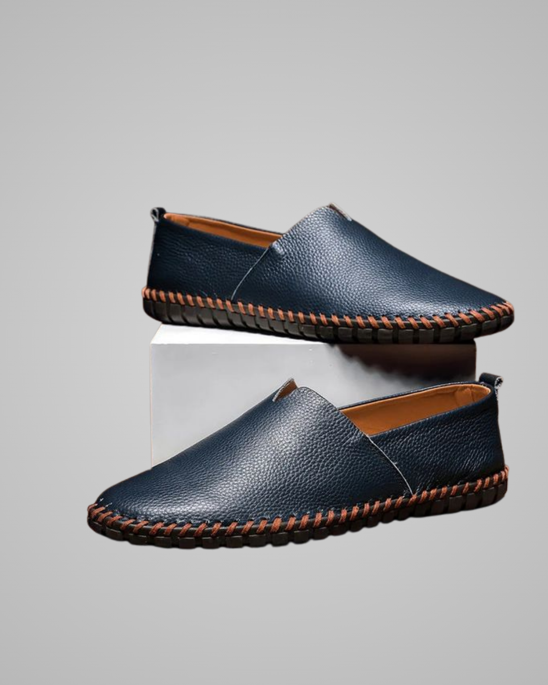 Pair of blue leather loafers with brown stitching on a gray background
