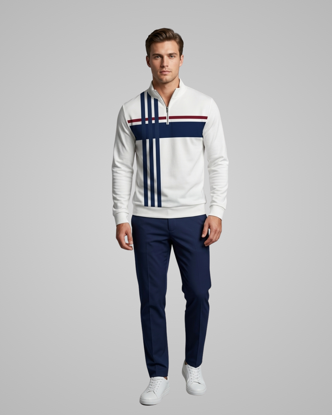Man wearing a white sweater with blue and red stripes and navy pants on a gray background