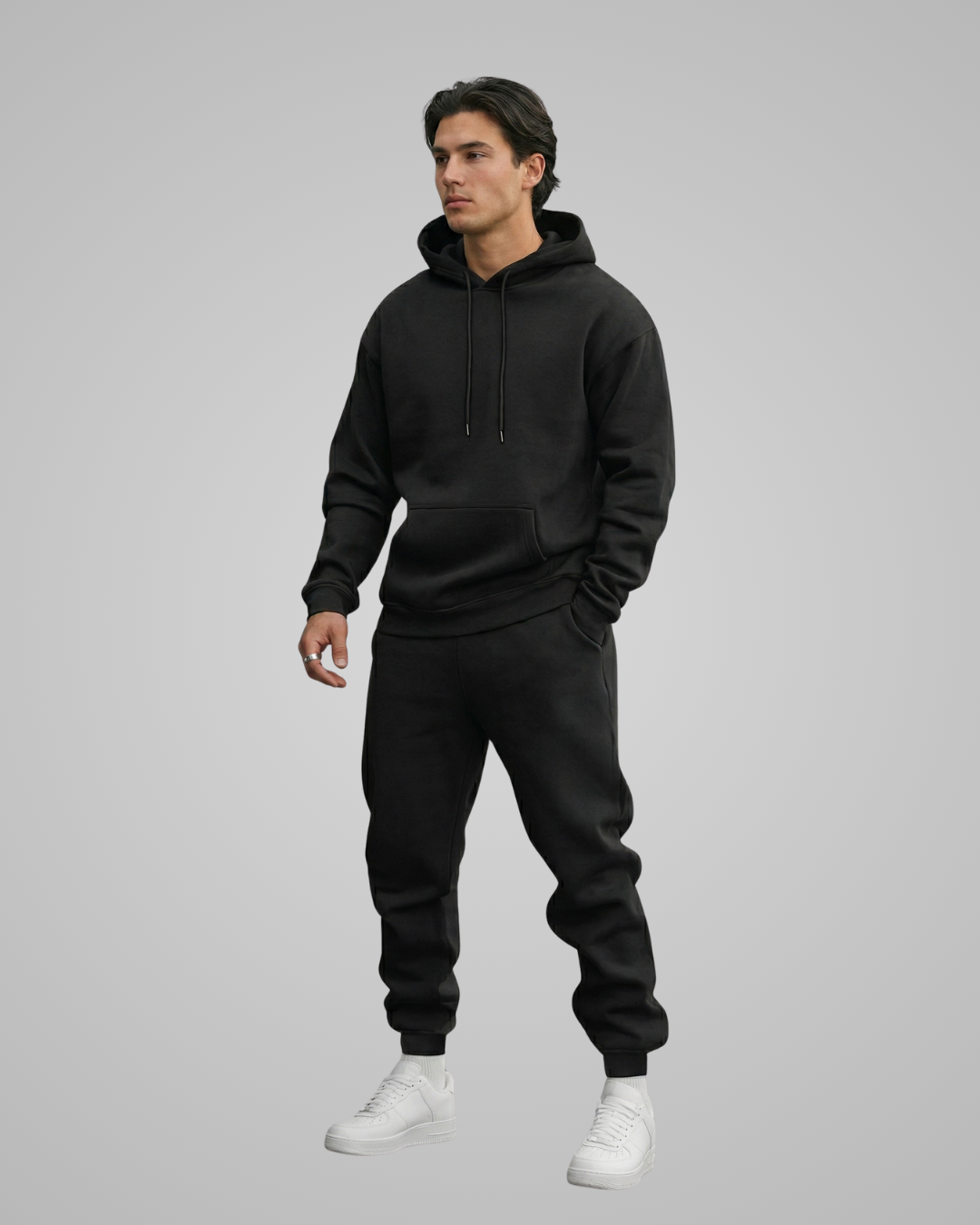 Person wearing a black hoodie and pants with white shoes on a gray background