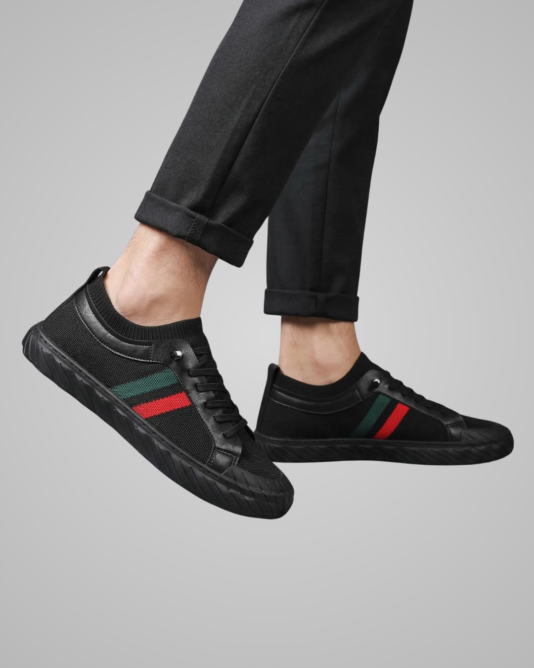 Black sneakers with red and green stripes worn by a person on a gray background