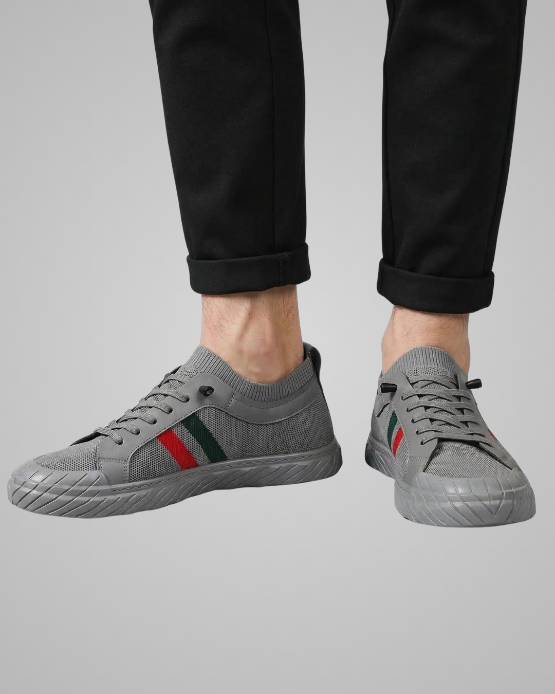 Gray sneakers with red and green stripes worn by a person on a gray background
