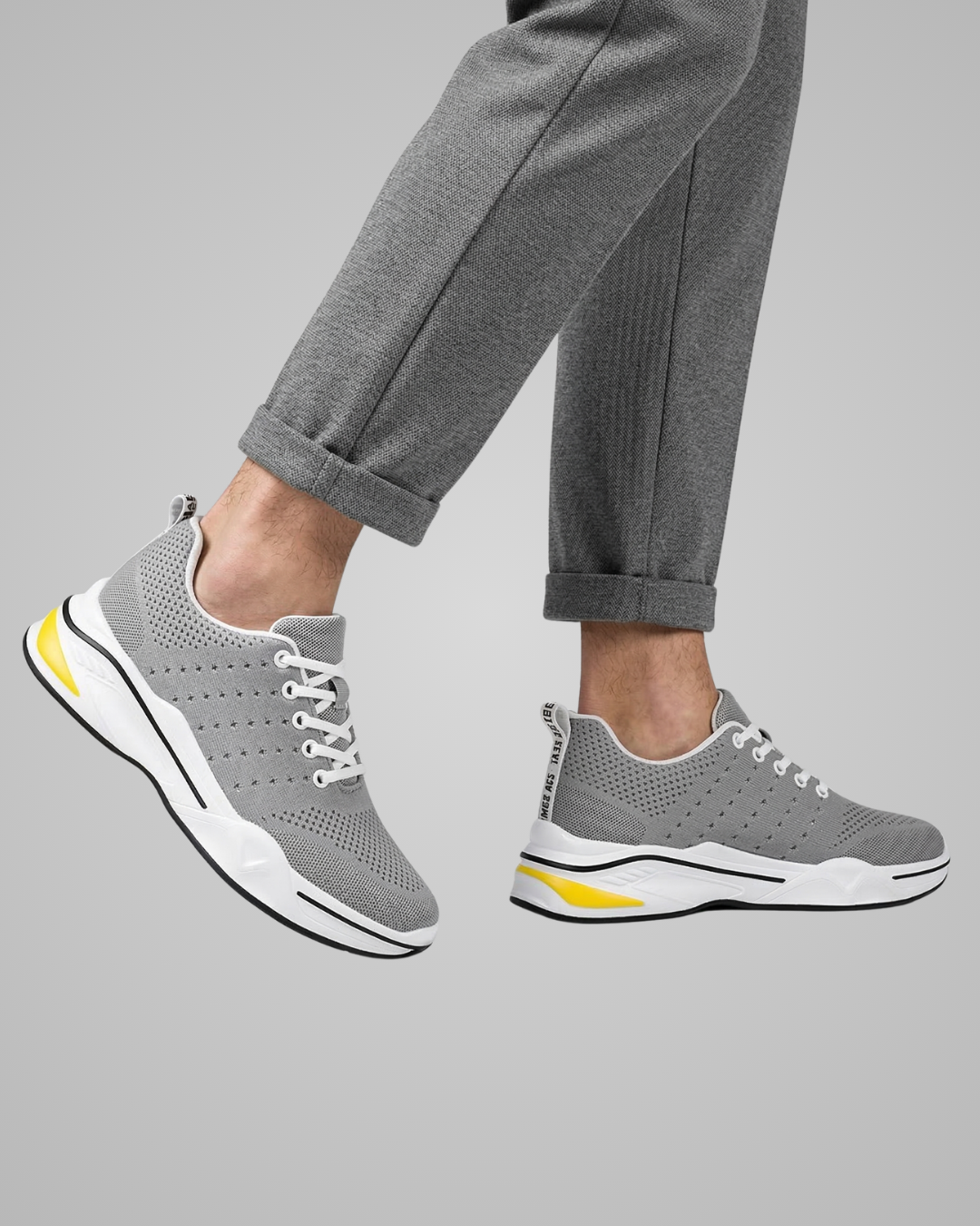 Gray sneakers with white soles and yellow accents worn with gray pants on a gray background