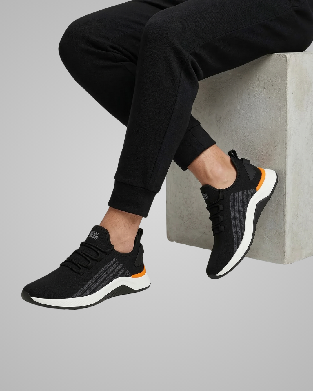 Person wearing black athletic shoes with white soles on a light gray background