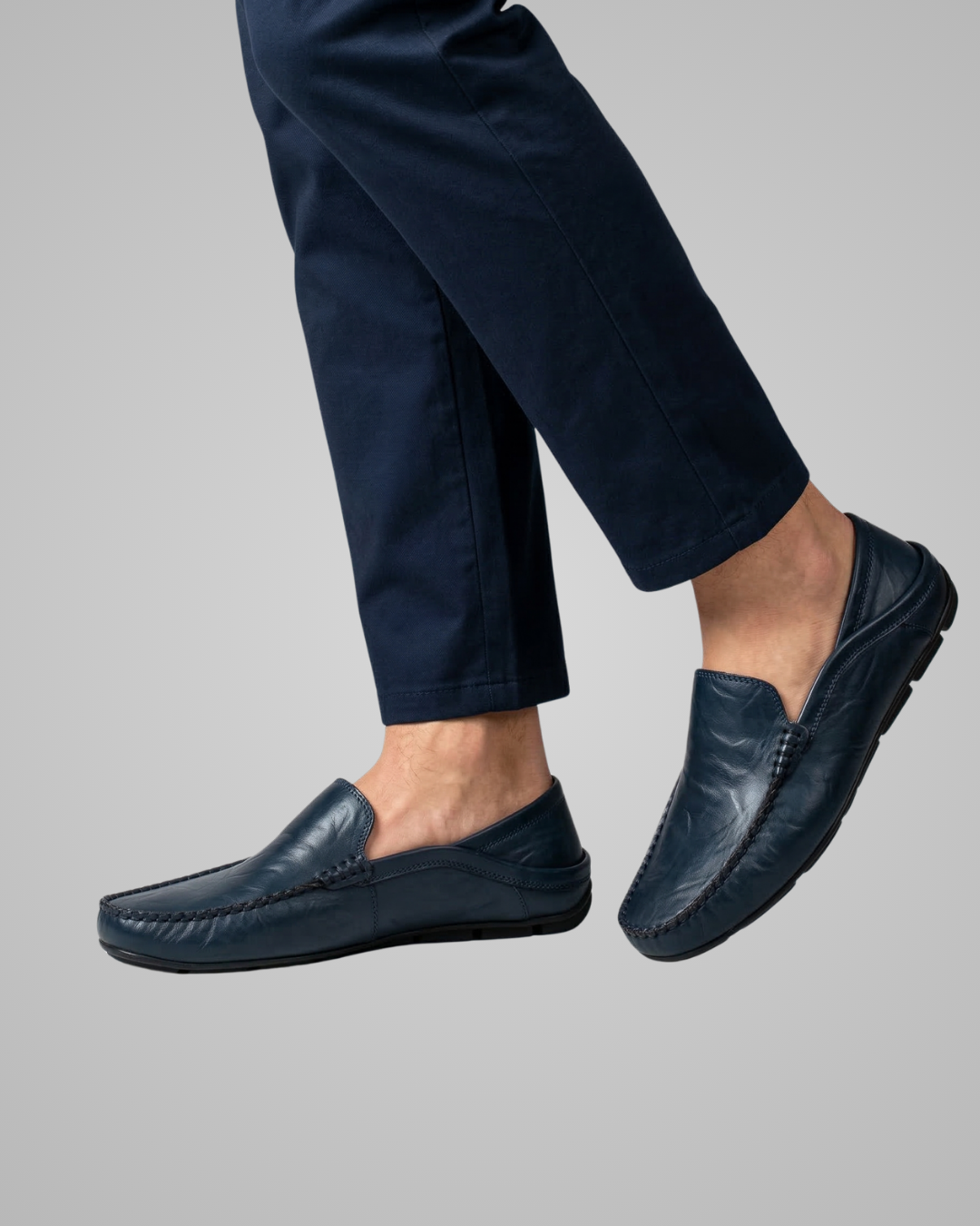 Navy loafers worn with navy pants on a gray background