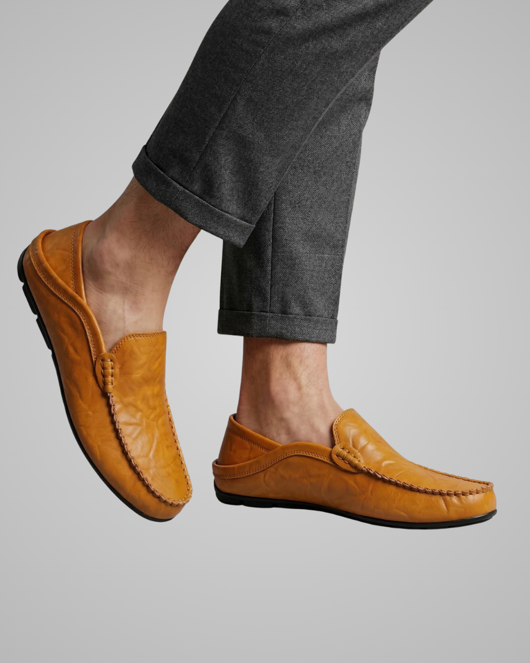 Brown leather loafers worn with gray pants on a plain background