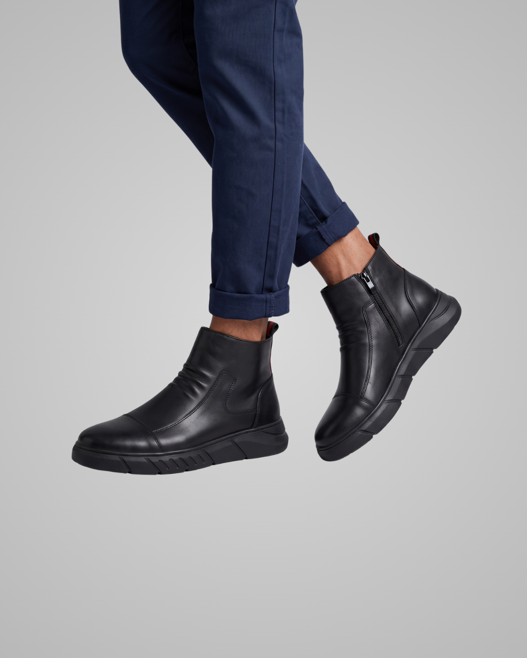 Black leather boots worn with navy pants on a gray background