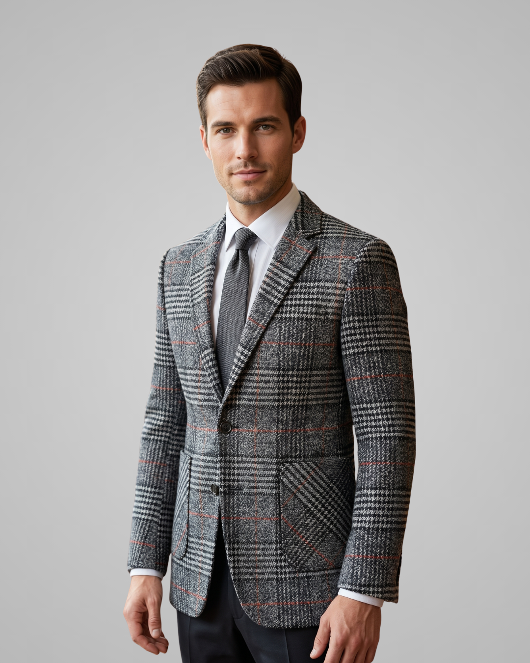 Man wearing a patterned blazer over a white shirt with a gray tie on a plain background