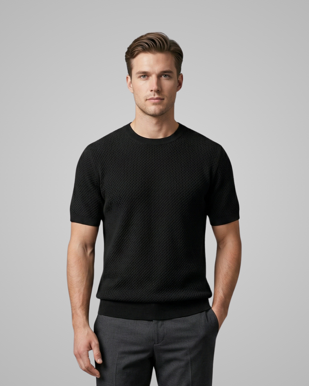 Man wearing a black textured sweater and gray pants on a gray background