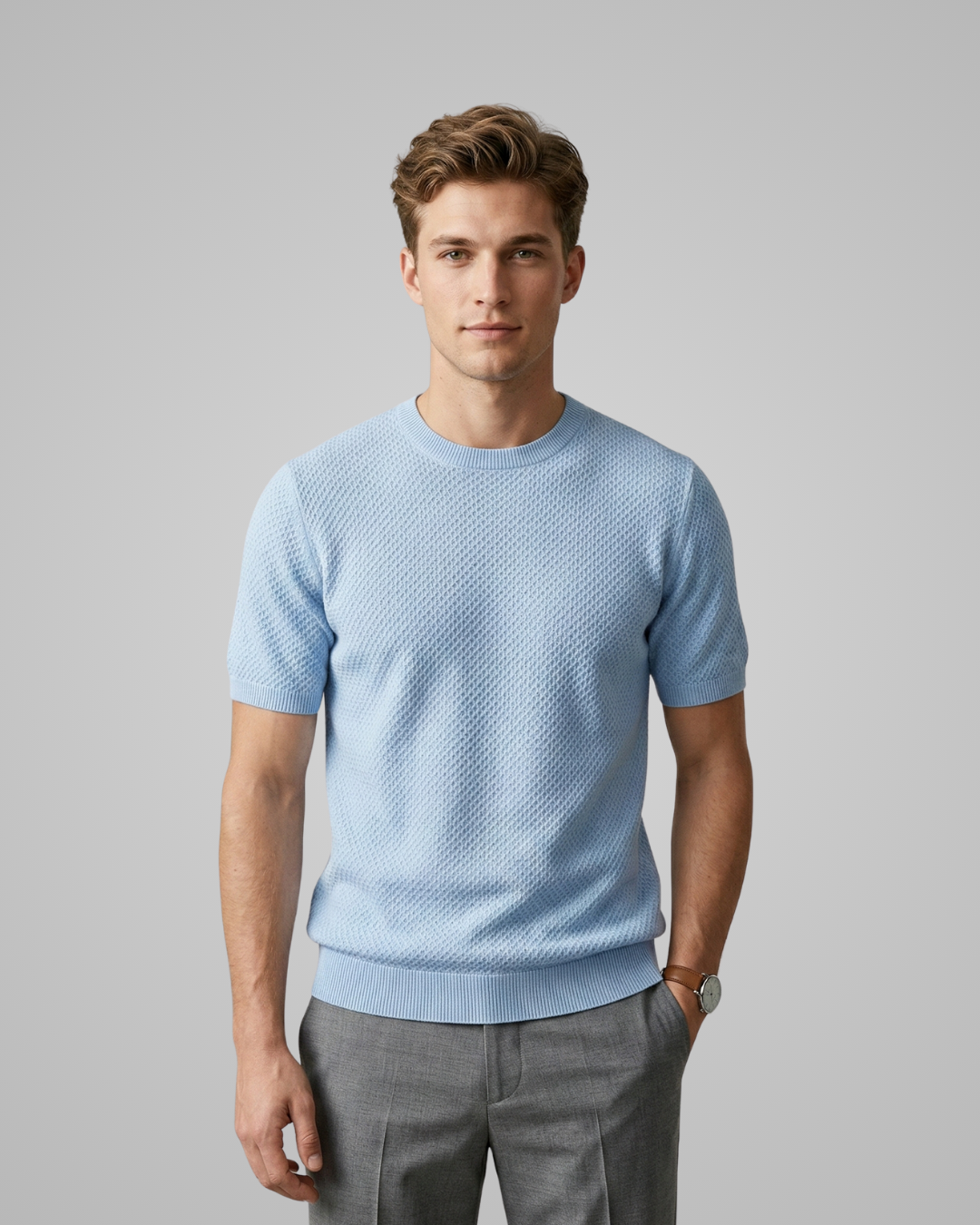 Man wearing a light blue textured shirt and gray pants on a gray background